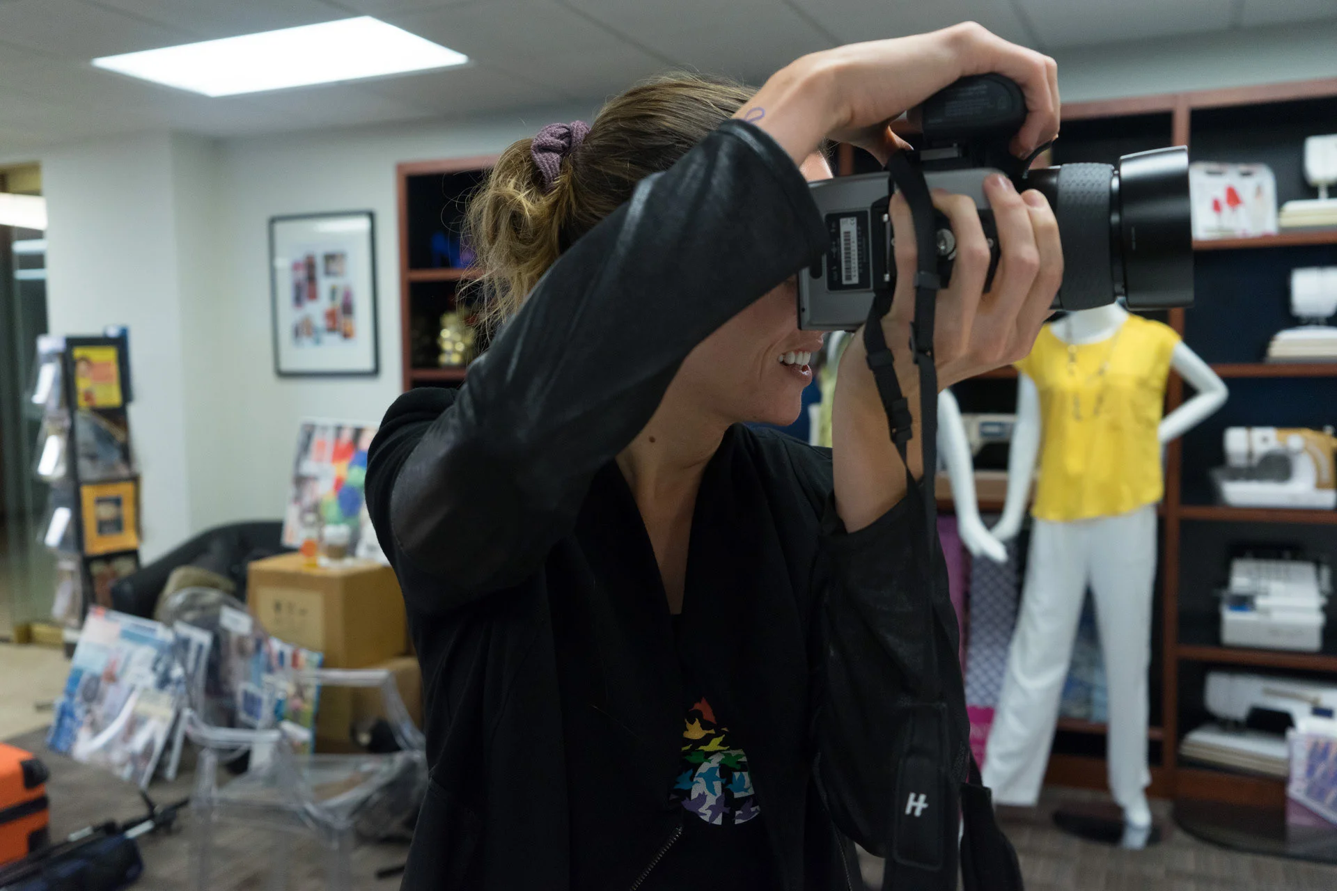 A photographer holding a camera to their eye inside a clothing studio.