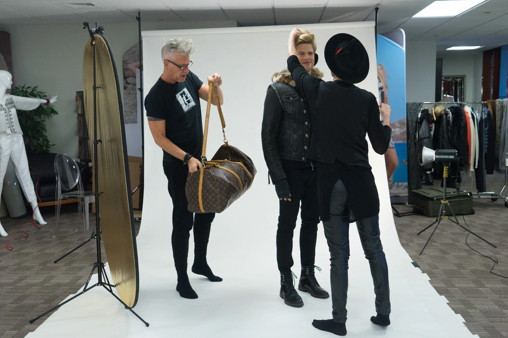 Three people arranging clothing and props on a white studio backdrop.