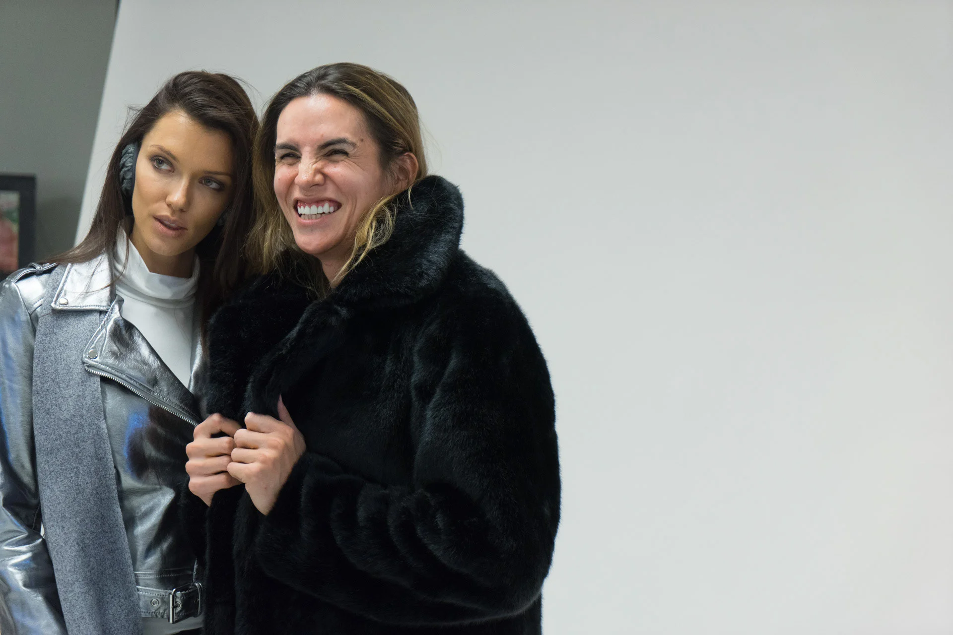 Two people posing together in silver and black outerwear against a gray background.