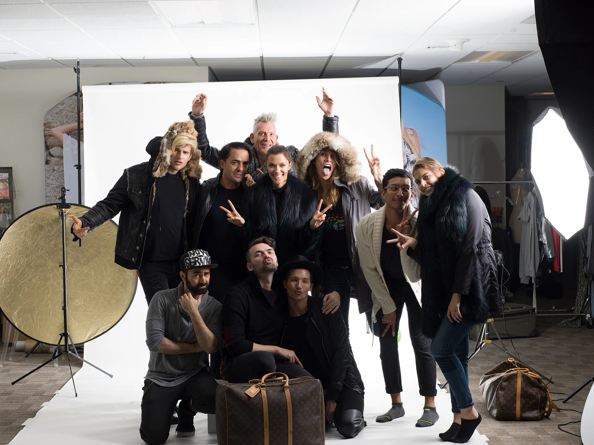 A group posing together with bags, lights and a white studio backdrop.