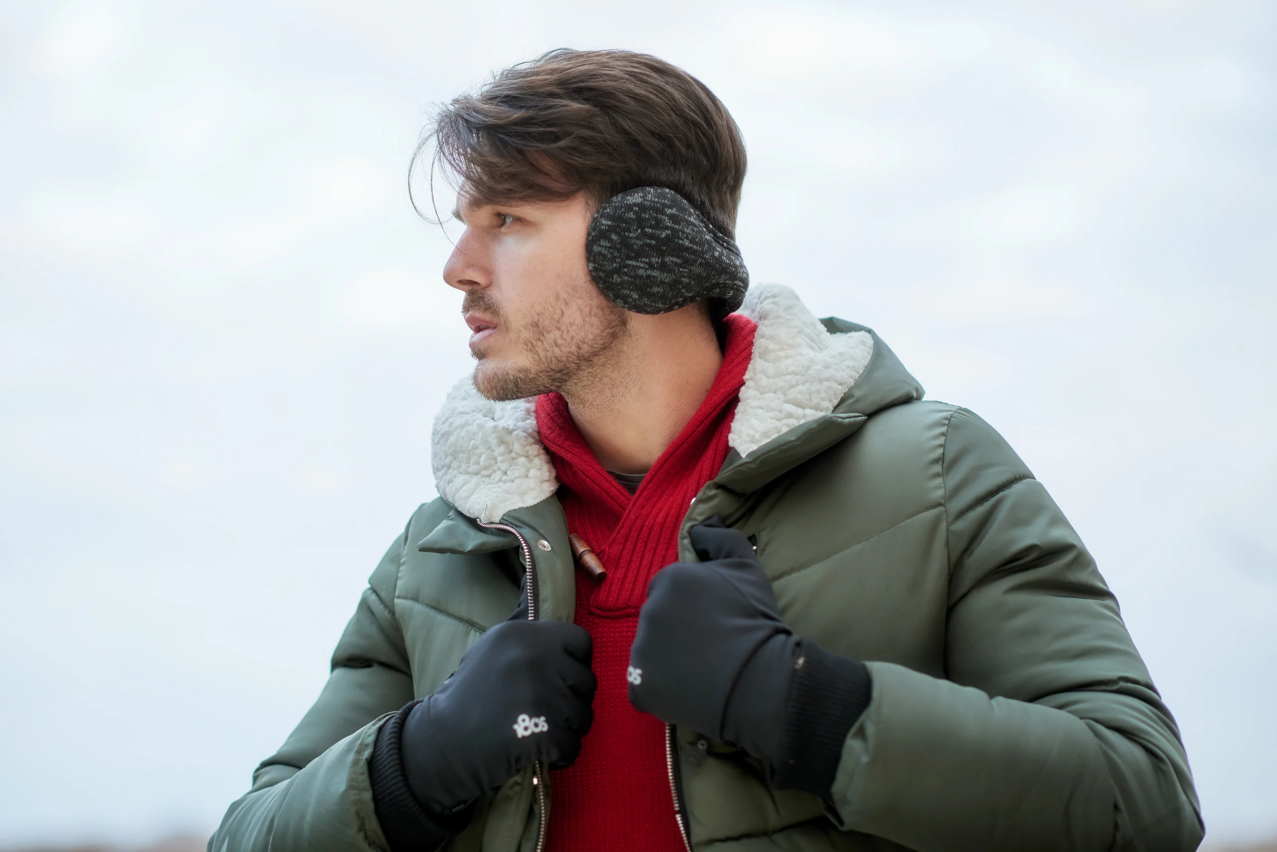 A model in black earmuffs, gloves and a green coat over a red sweater.