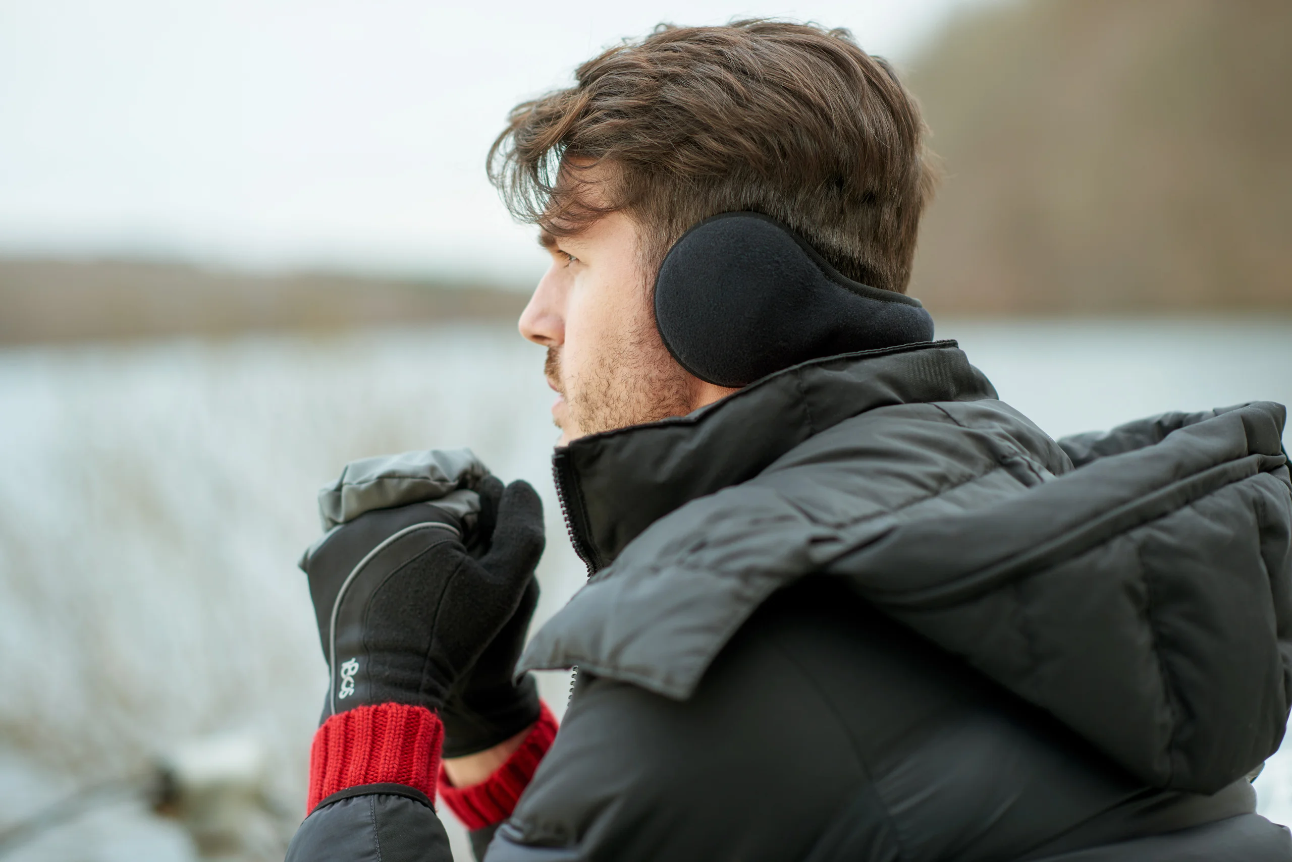 A side portrait of a model in black earmuffs and gloves, with a red knitted cuff.