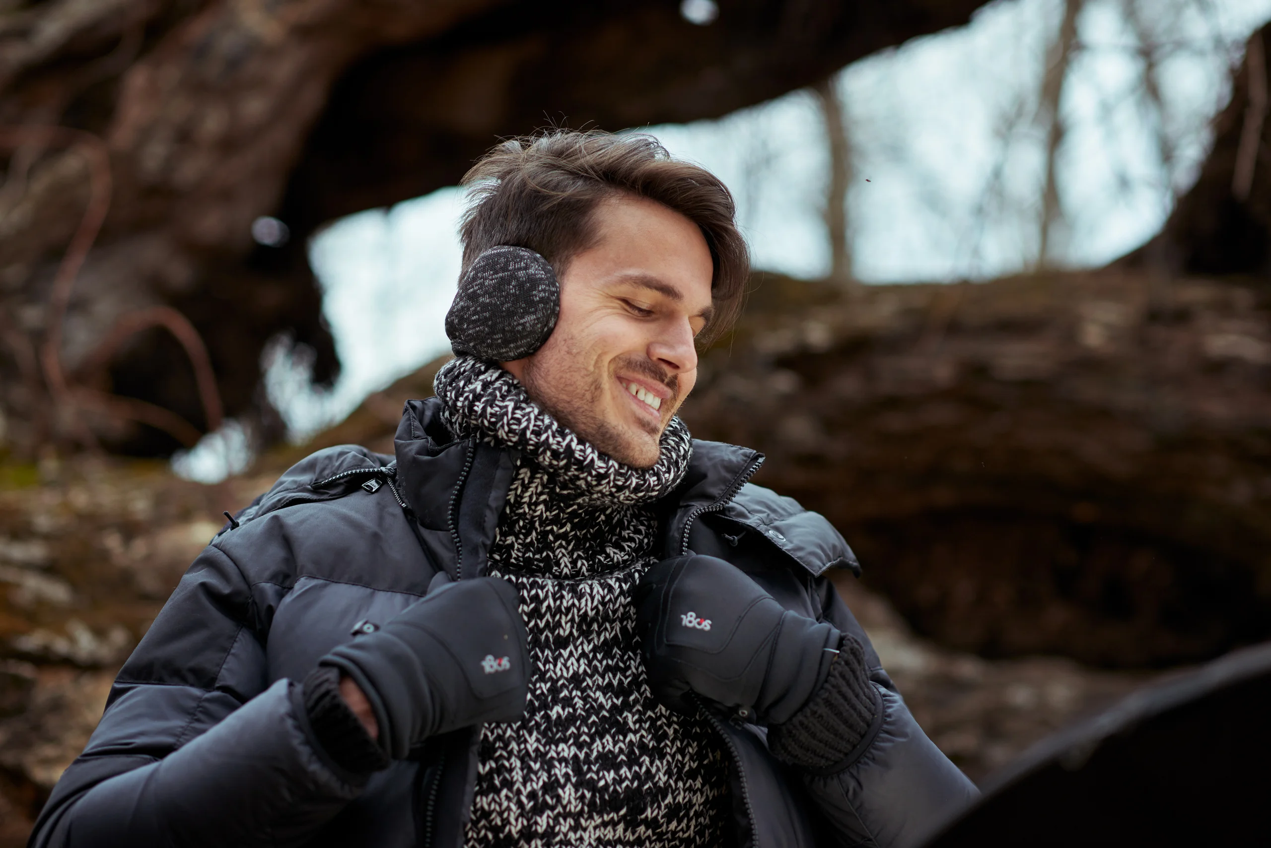 A smiling model in gray earmuffs, a patterned scarf and a padded jacket.