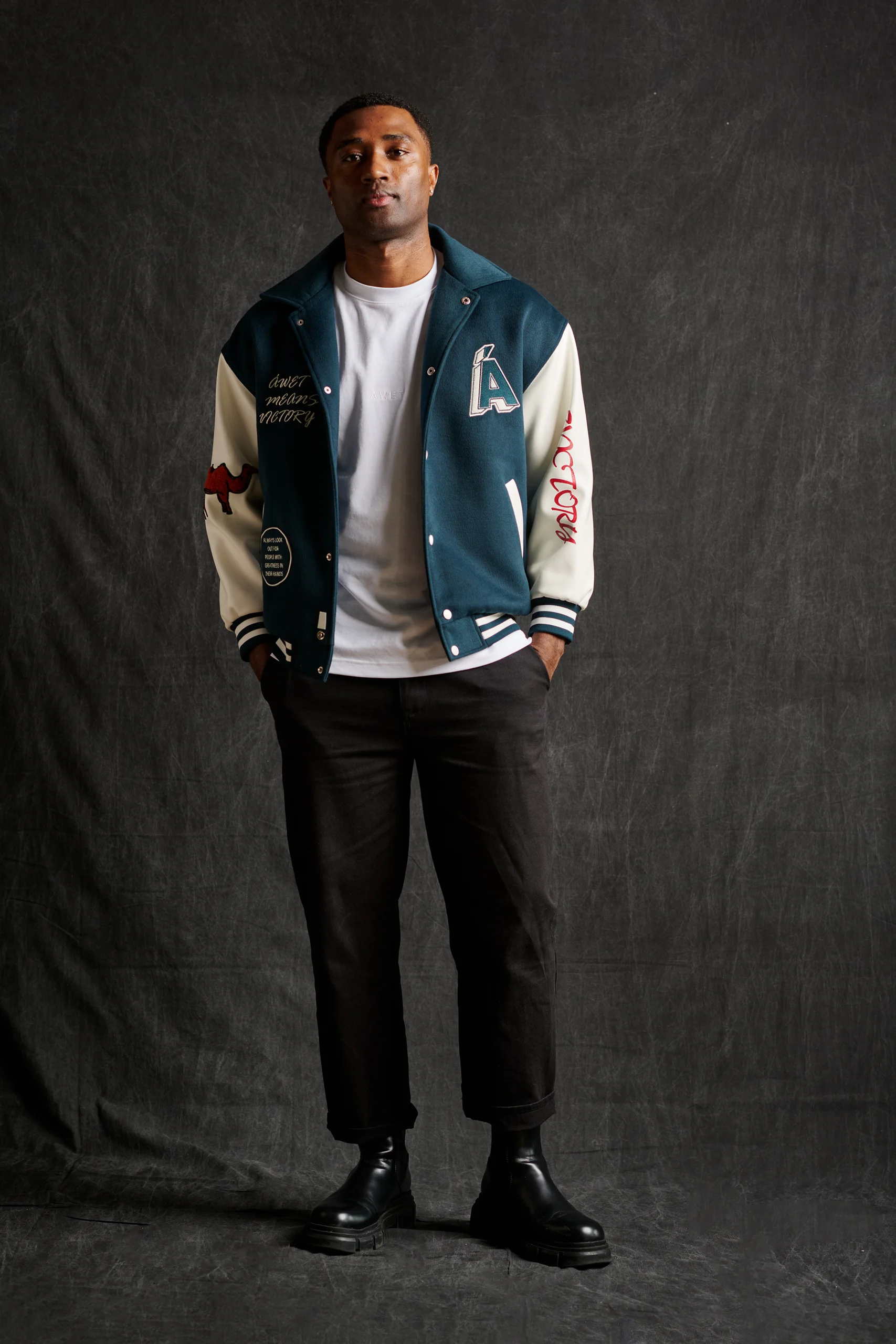 A model in a blue-and-cream varsity jacket over a white shirt and black trousers.
