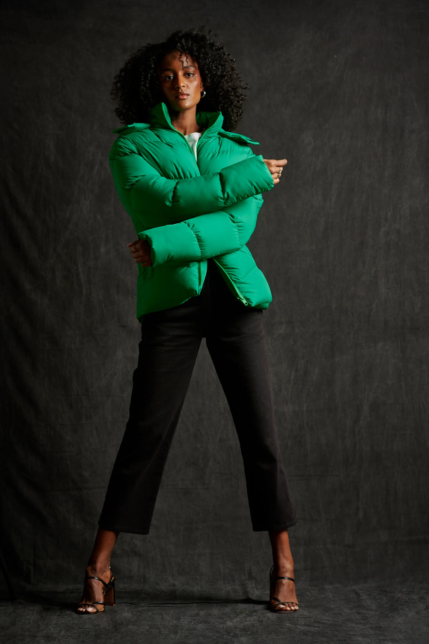 A model in a vivid green jacket and black trousers against a dark backdrop.