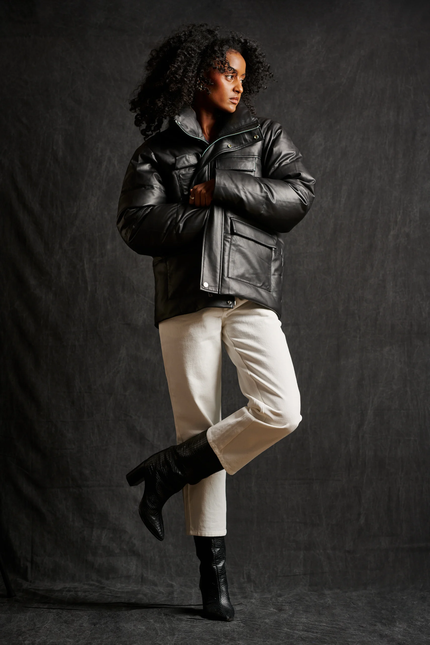 A model in a black padded jacket and cream trousers balancing with one leg bent.