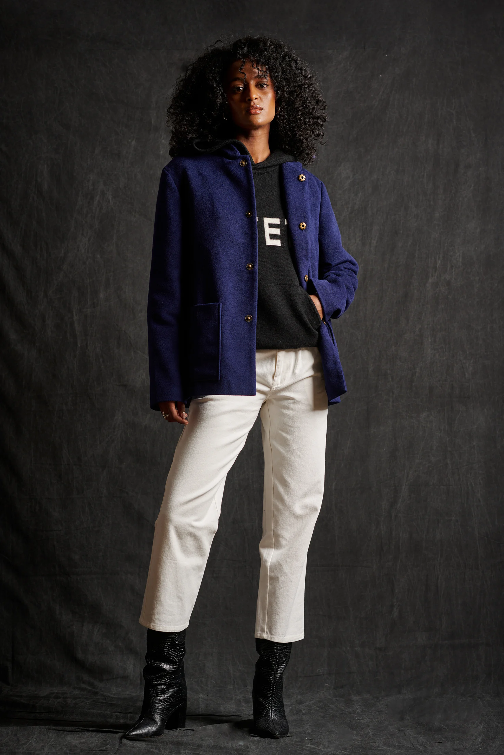 A model wearing a blue jacket, black shirt and cropped white trousers.