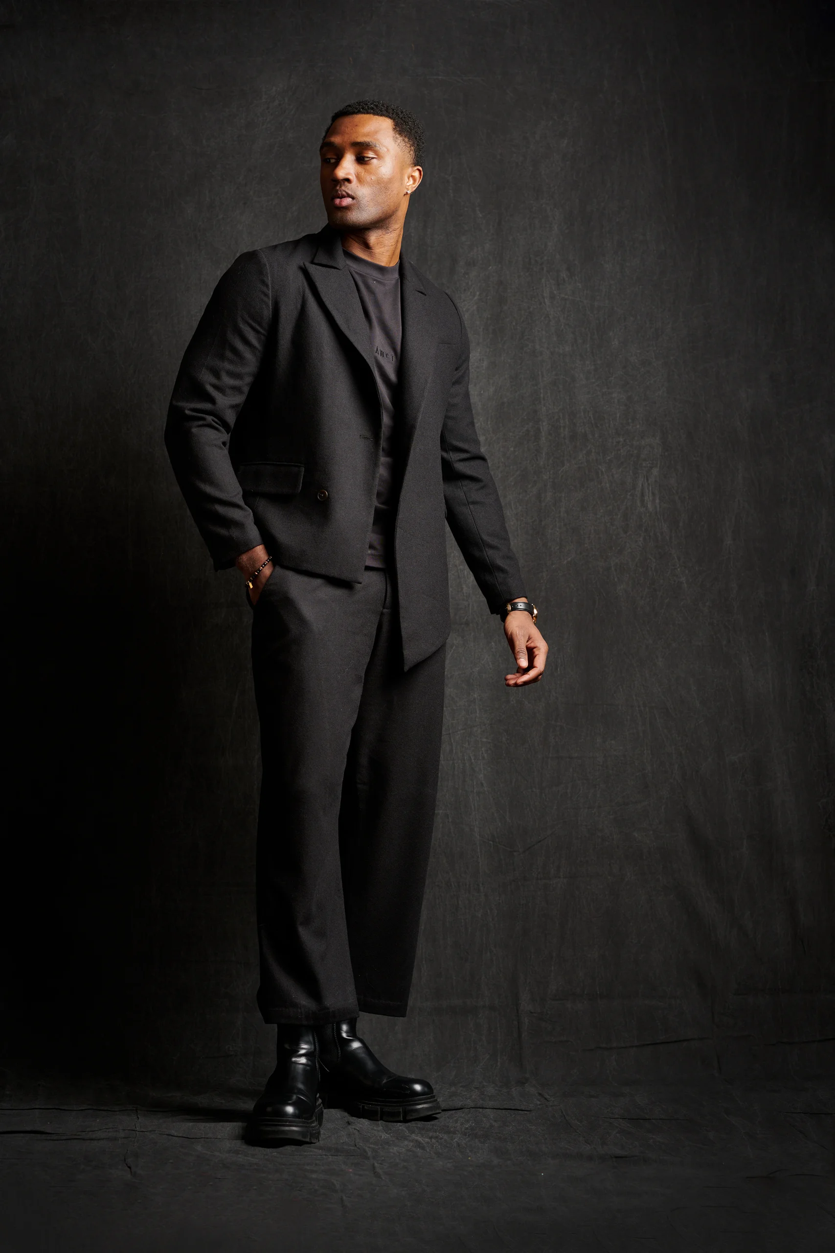 A model in an all-black suit looking upward to the side.