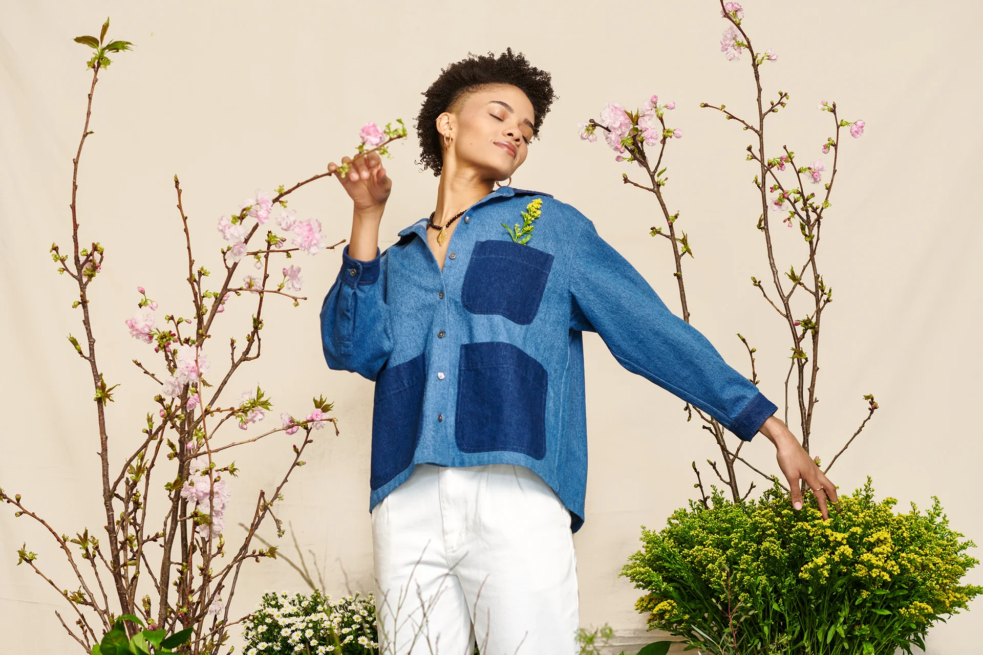 A model in a blue shirt reaching toward the surrounding greenery.