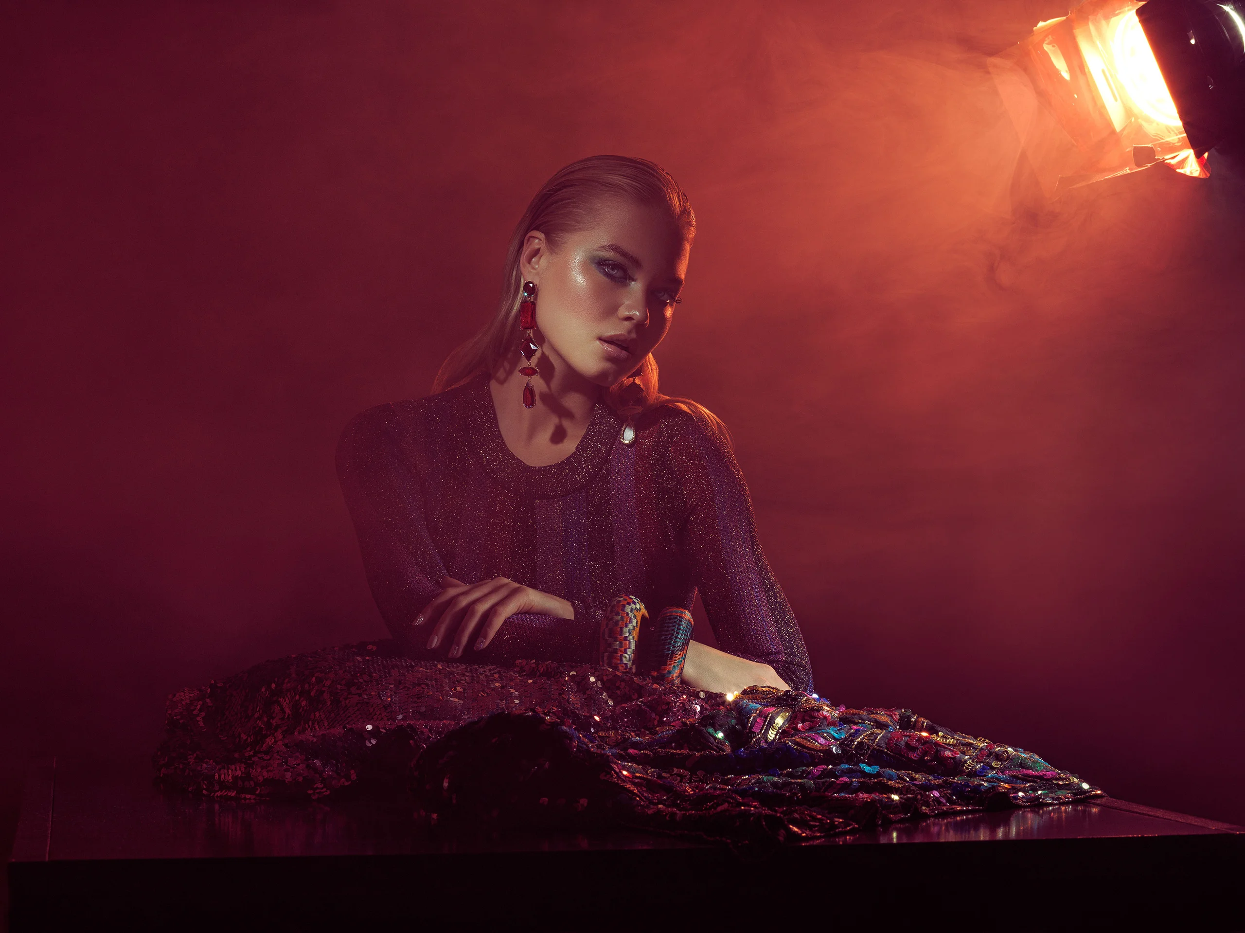 A model seated at a table under red light and haze.