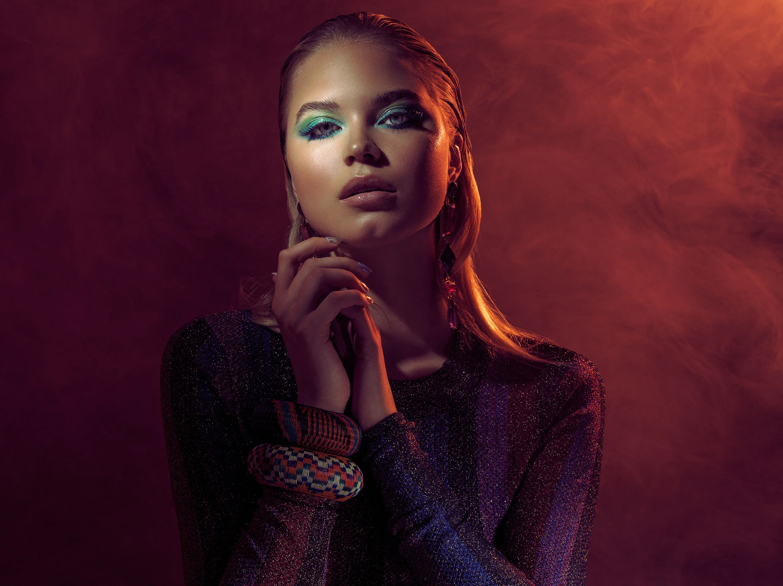A beauty portrait with jewelry and a hand against the face in violet and red light.