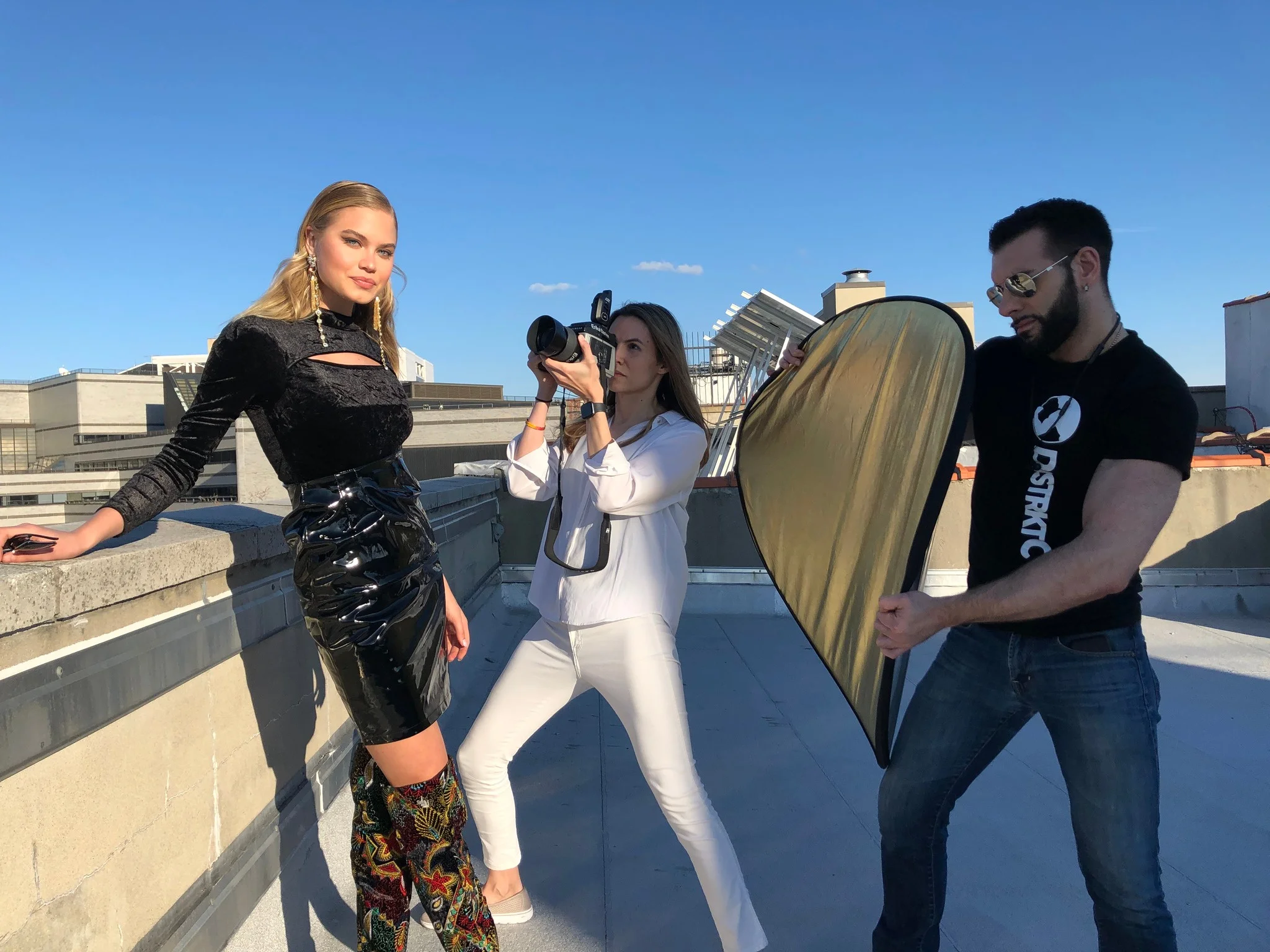 Behind the scenes on a rooftop with a model, photographer, and reflector.