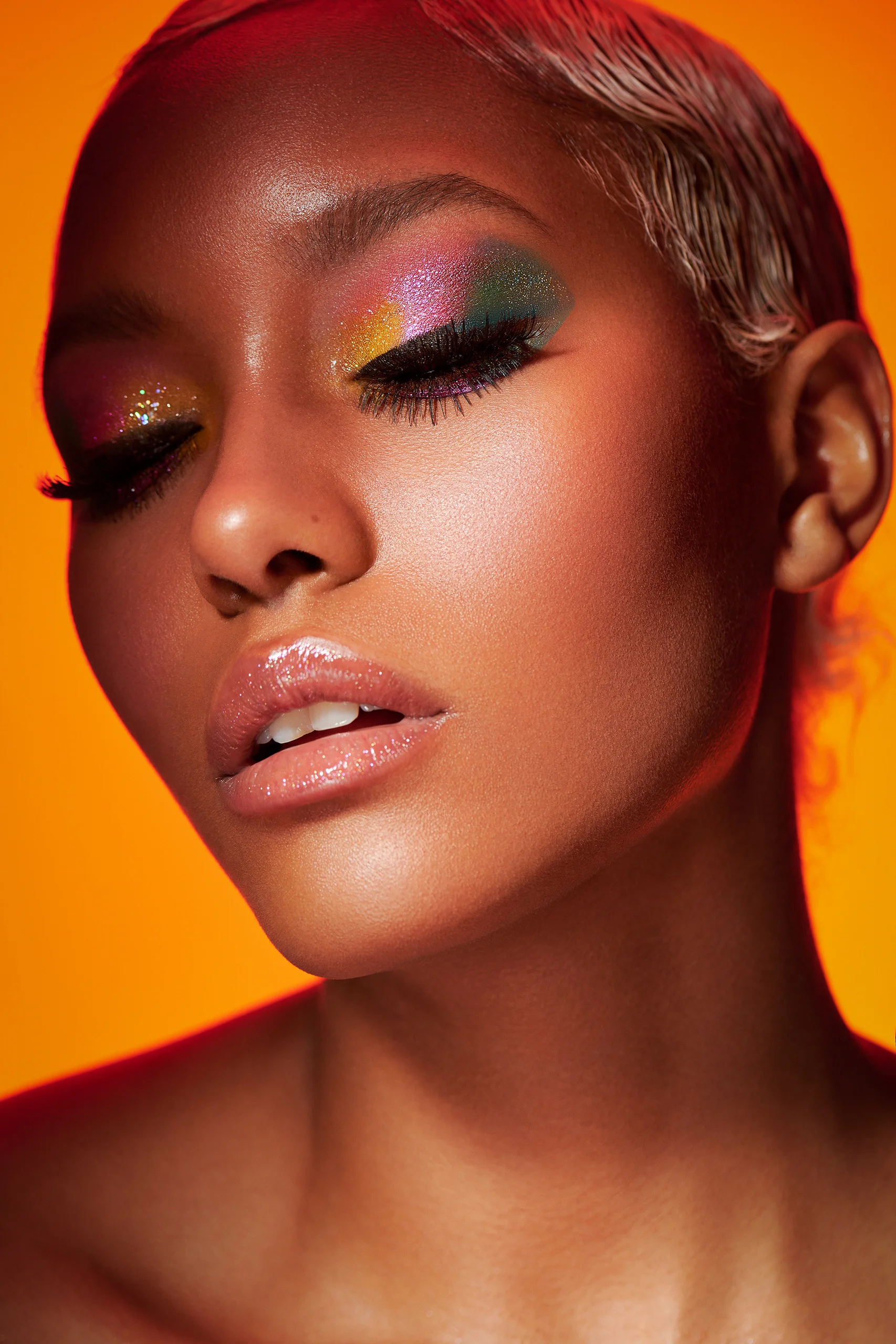 A beauty portrait with closed eyes and multicolored eye makeup against orange.