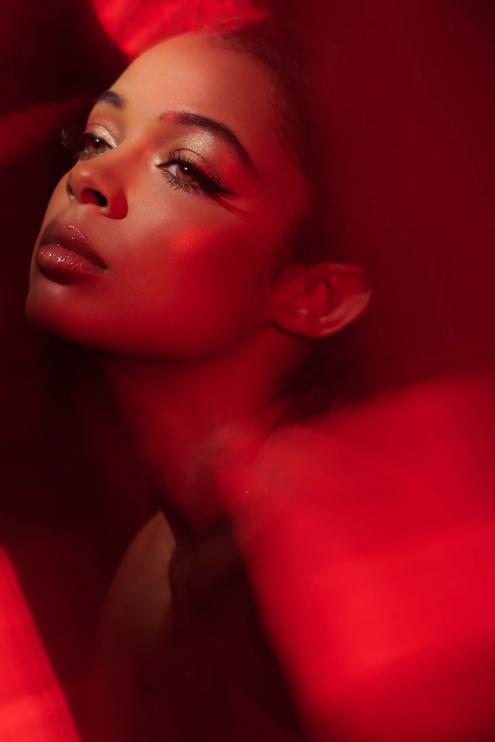 A beauty portrait with shimmering makeup and translucent red reflections.