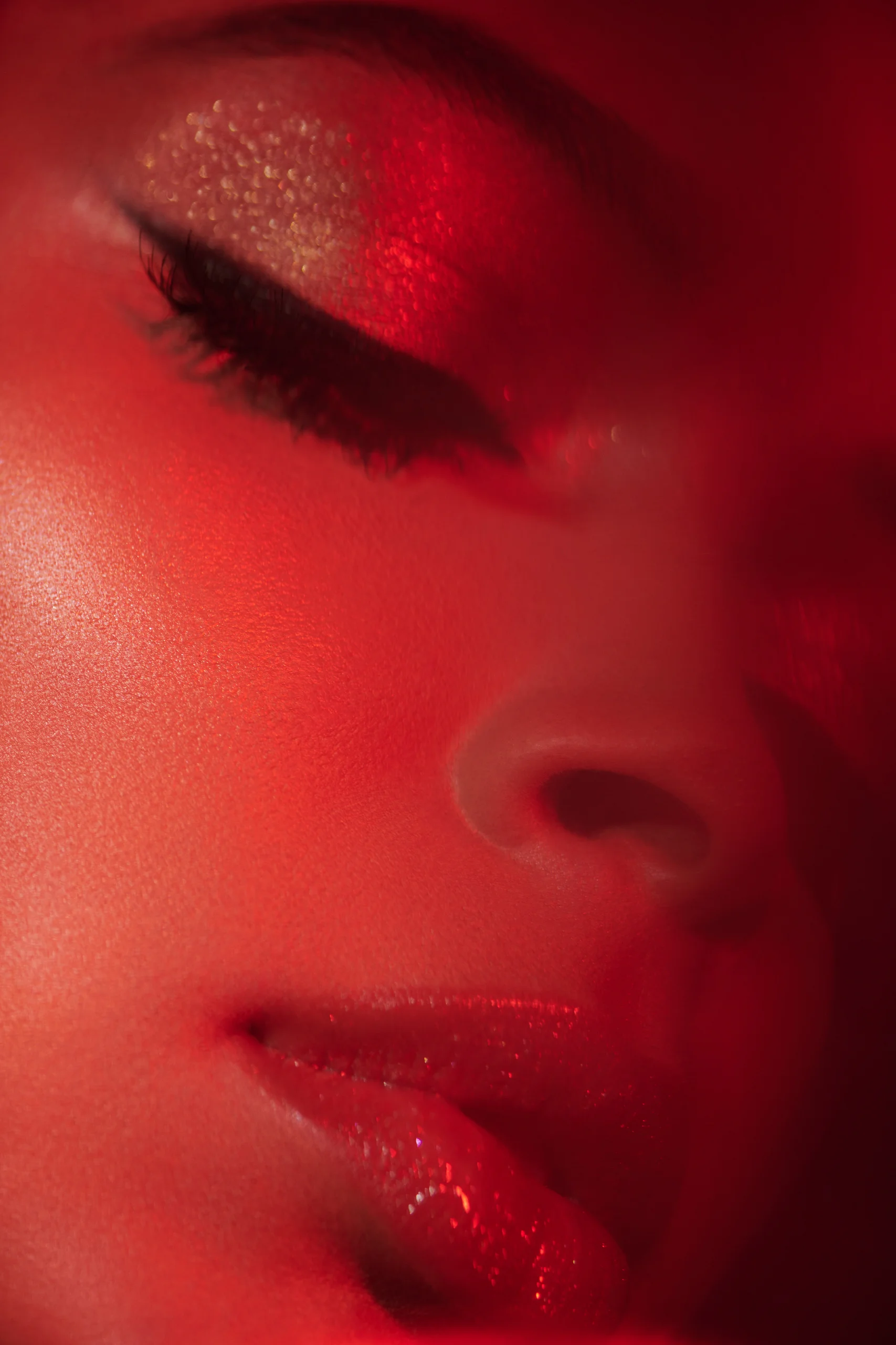 A close-up of glittering eye makeup and lips in red light.