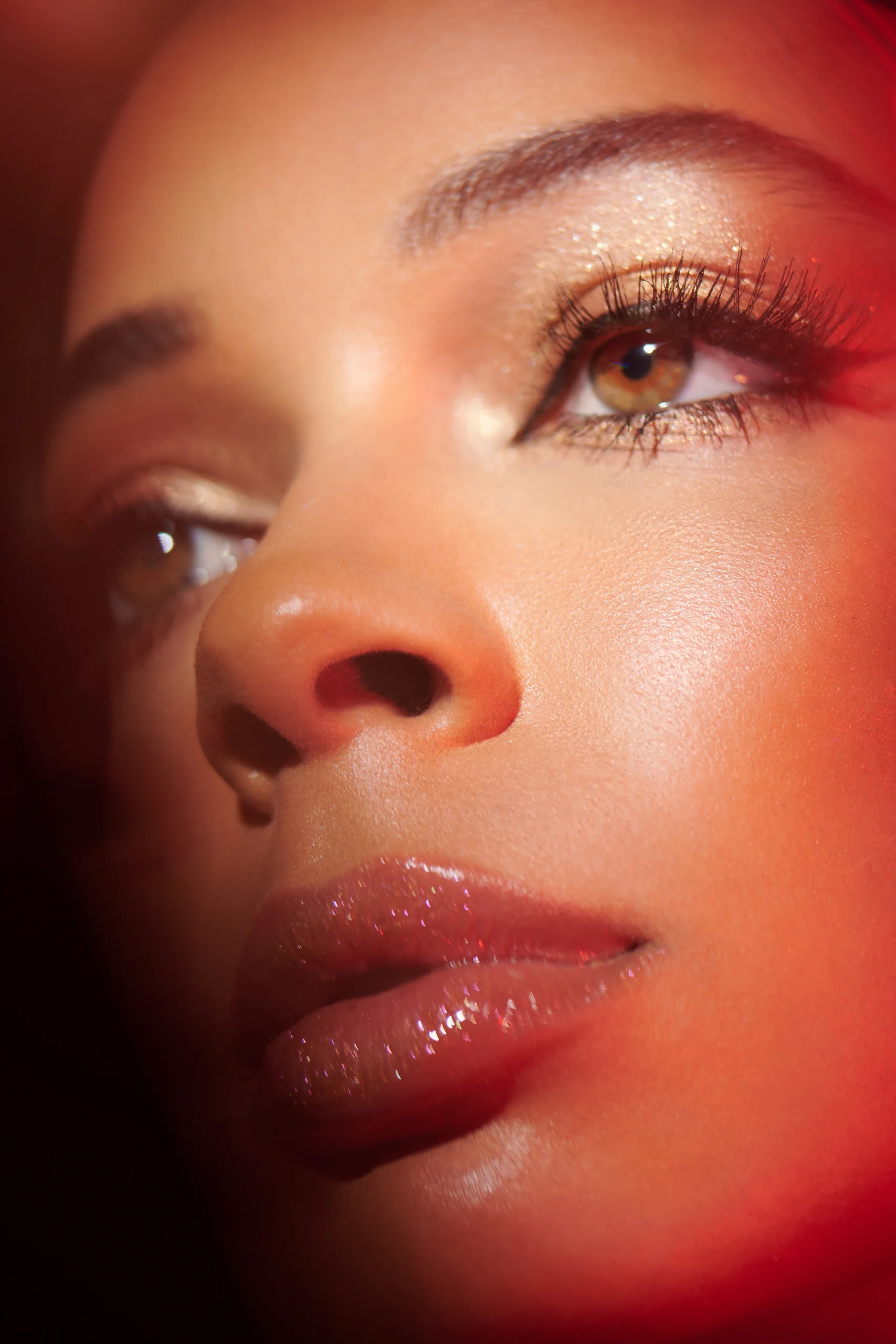 A close beauty portrait with gold makeup and a warm red edge of light.