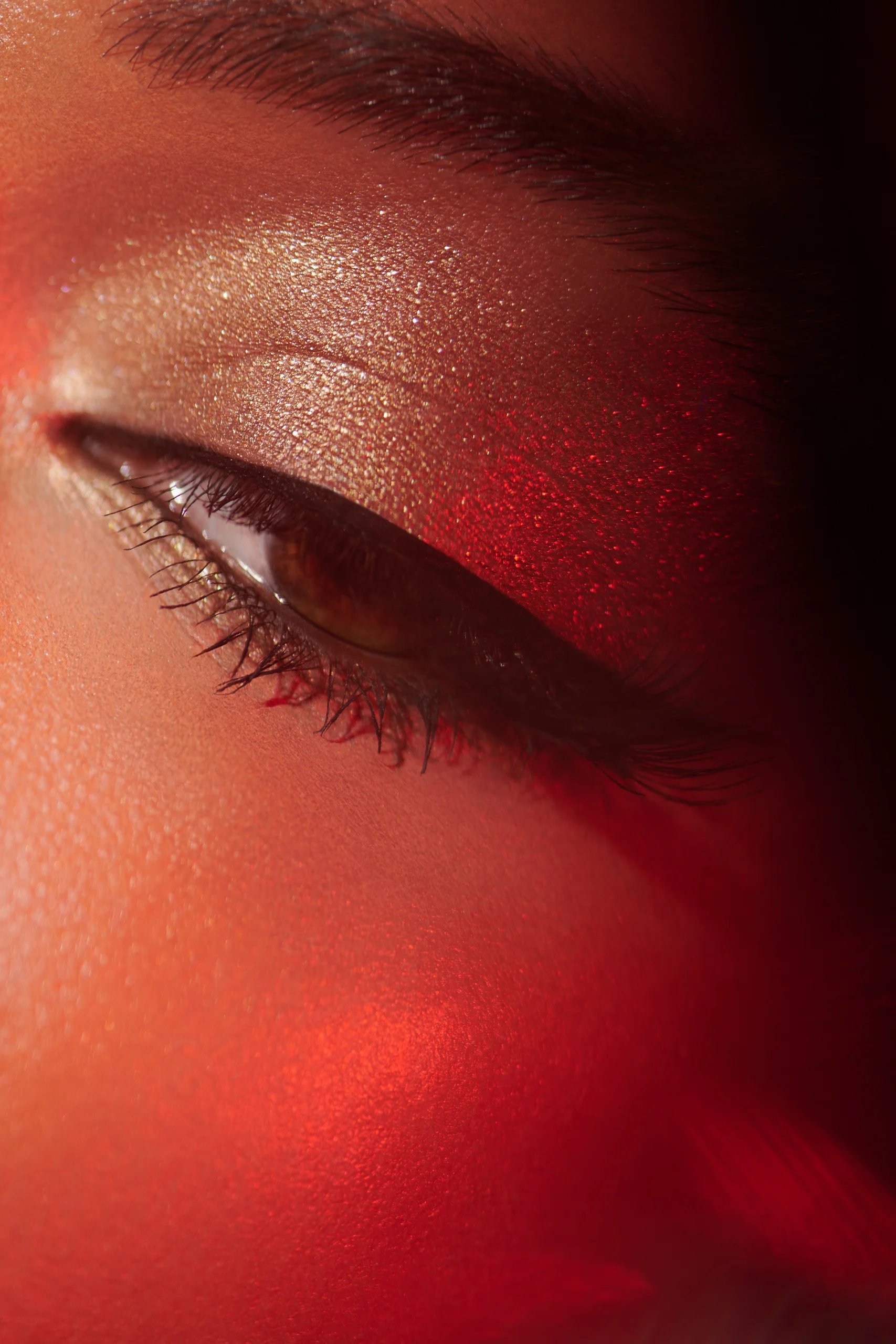 A detail of closed eyes with shimmering pale makeup and red light.