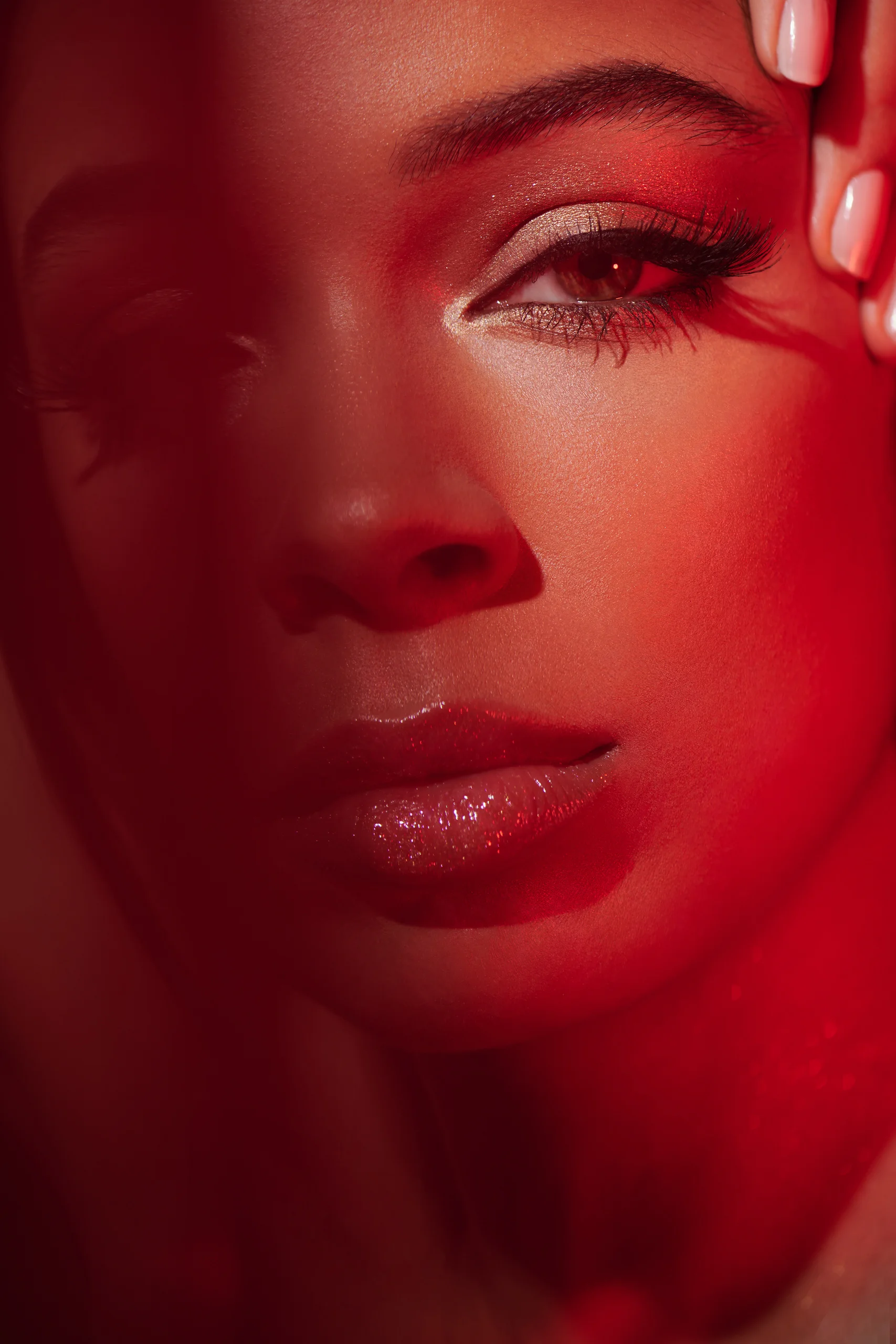 A close beauty portrait with a hand at the temple against red light.