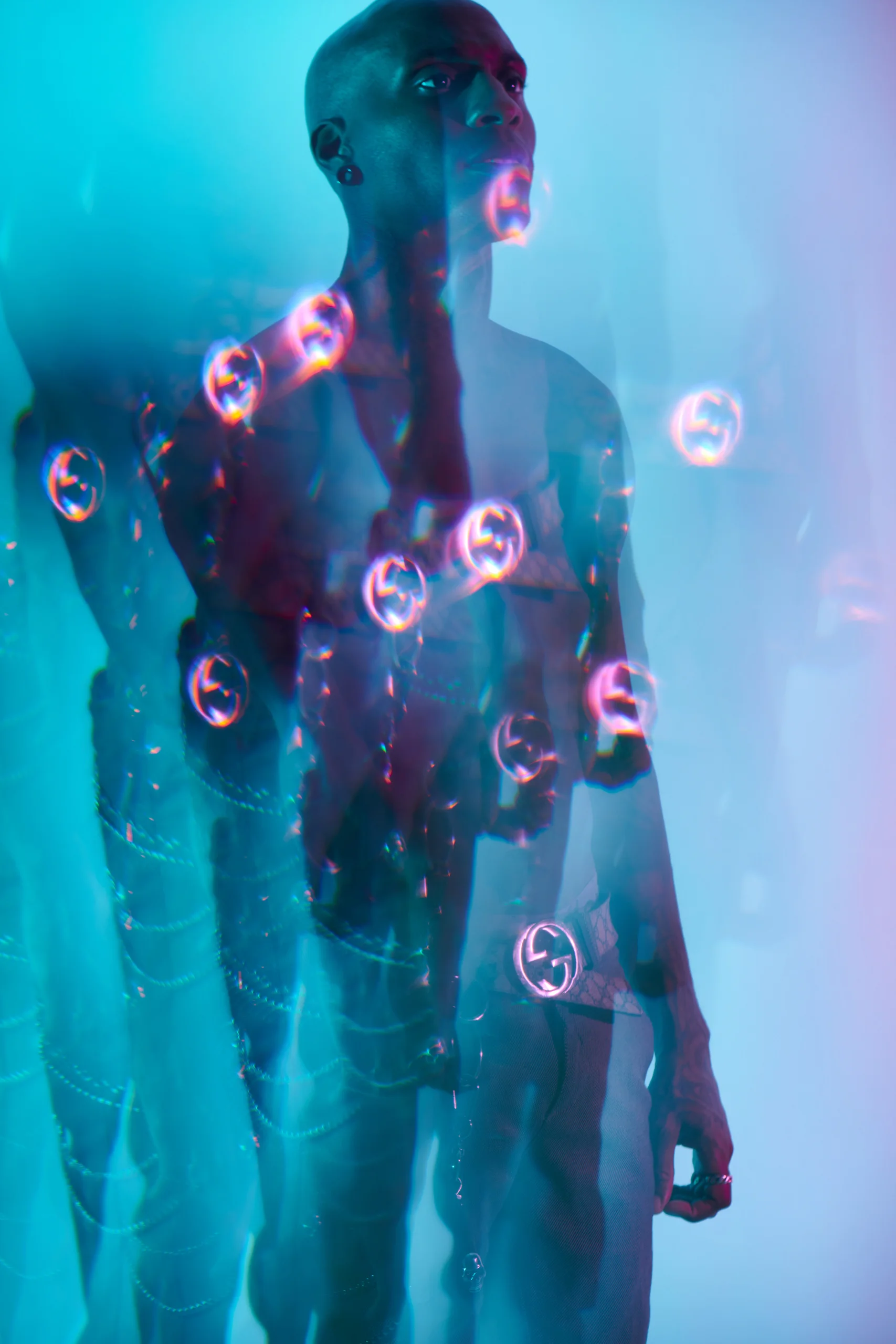 A standing figure under blue light, with bubbles and overlapping translucent silhouettes.