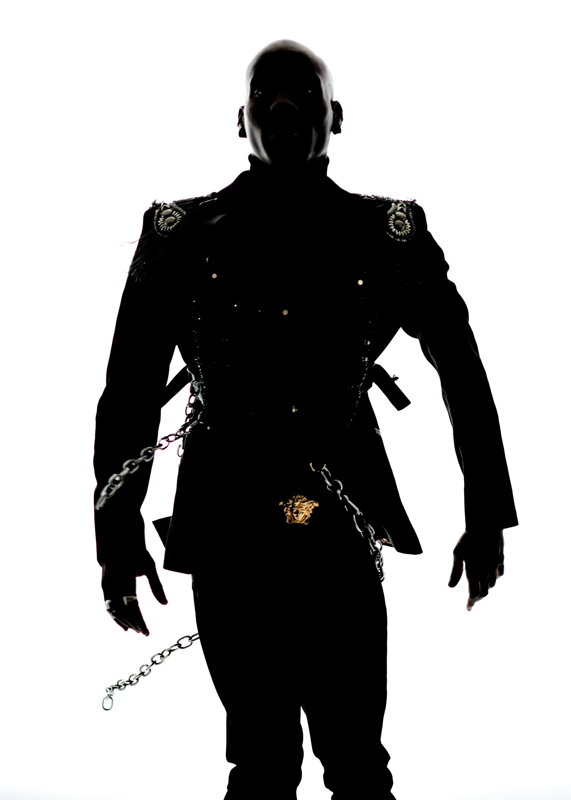 A front-facing silhouette in a fitted dark jacket, with chains catching the light.