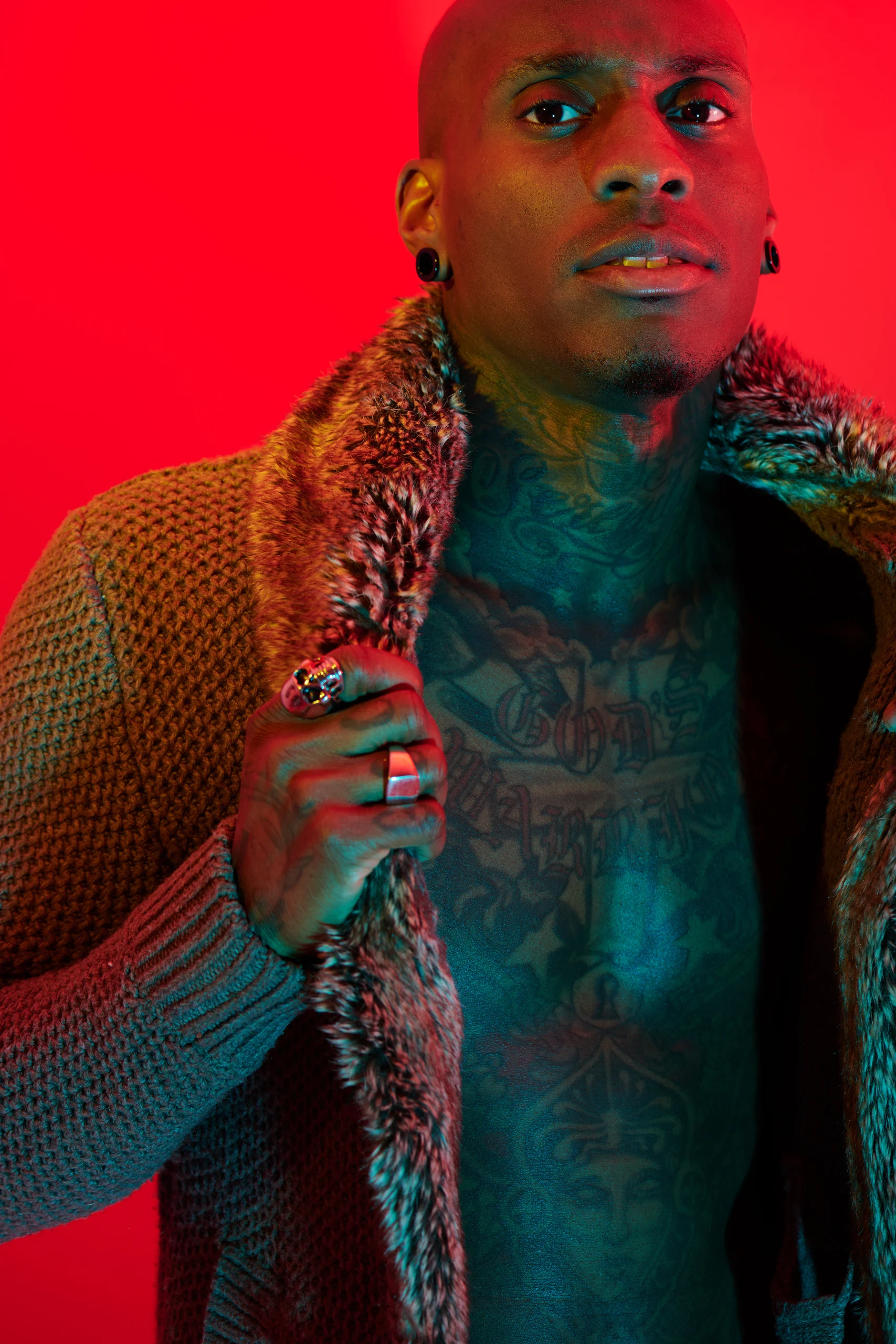 A close portrait of a model gripping a patterned coat lapel against bright red.