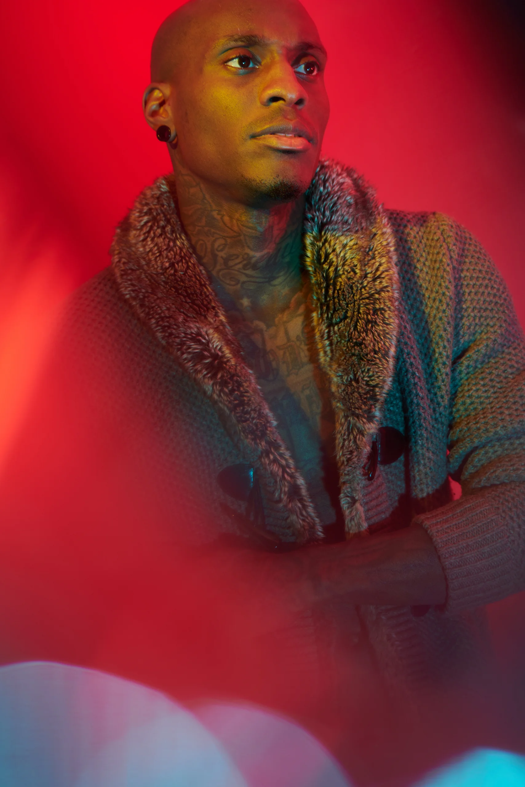 A model in a textured coat looking upward through soft red and blue reflections.