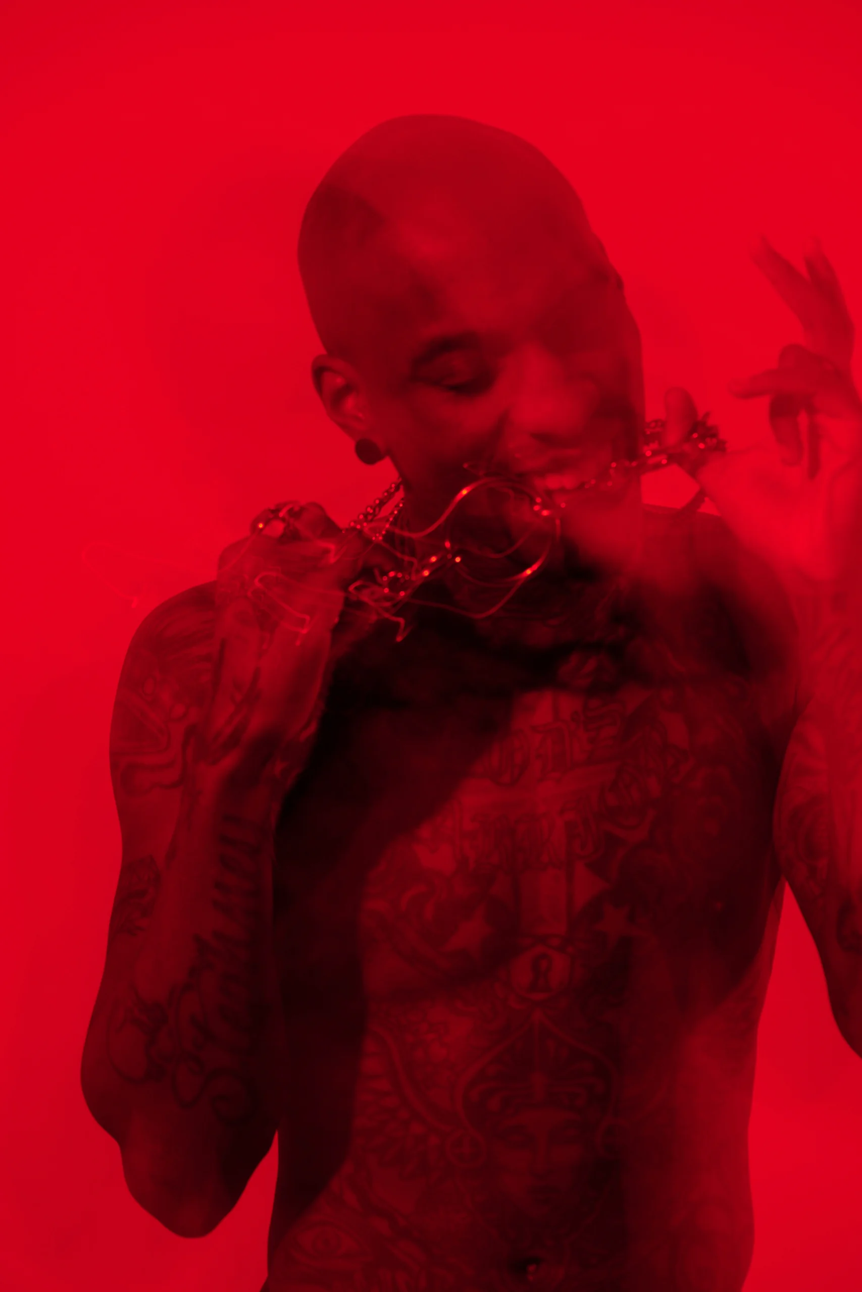 A bare-chested figure holding a chain near the mouth under saturated red light.