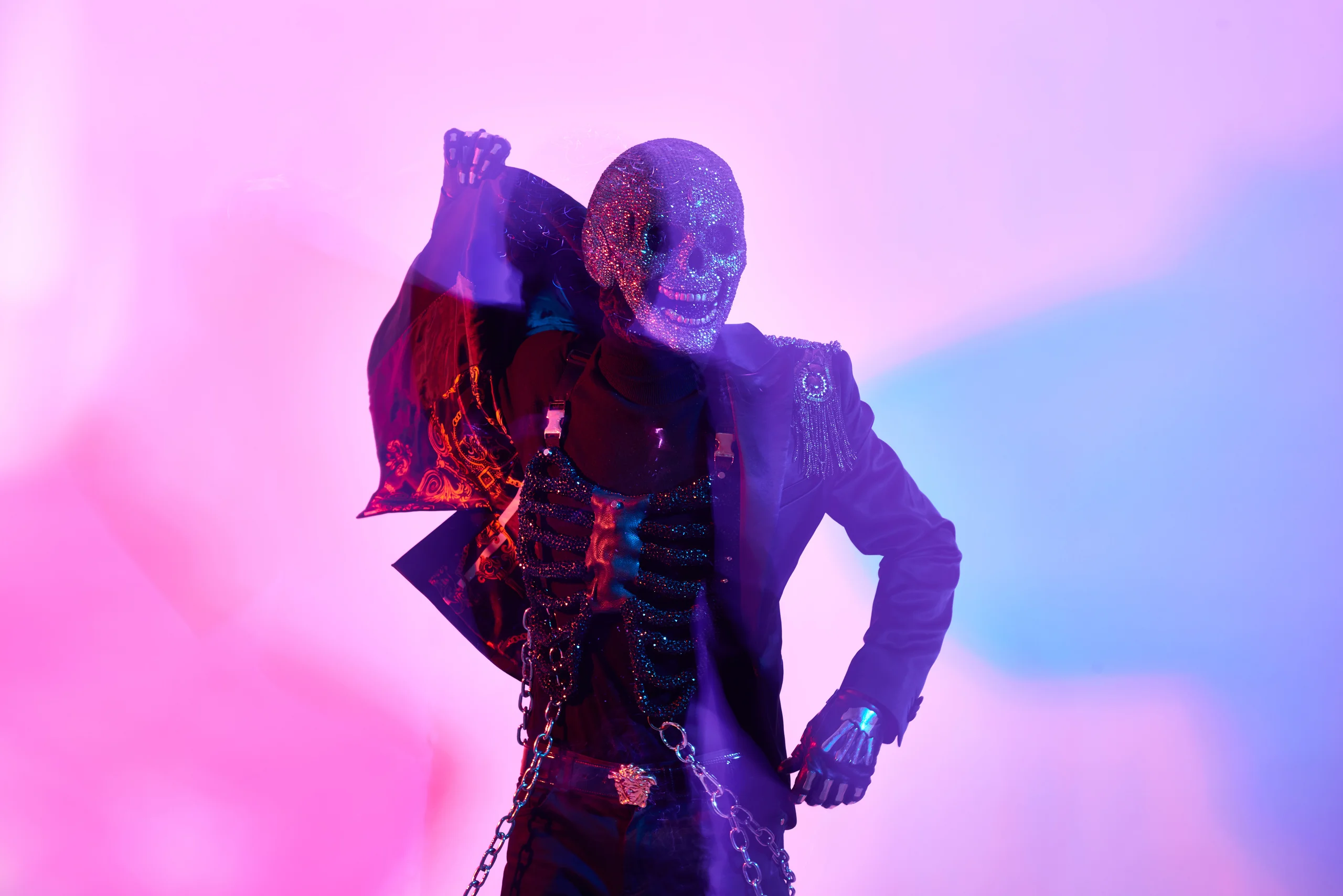 A figure in a dark jacket with one arm raised, surrounded by pink and blue shadows.