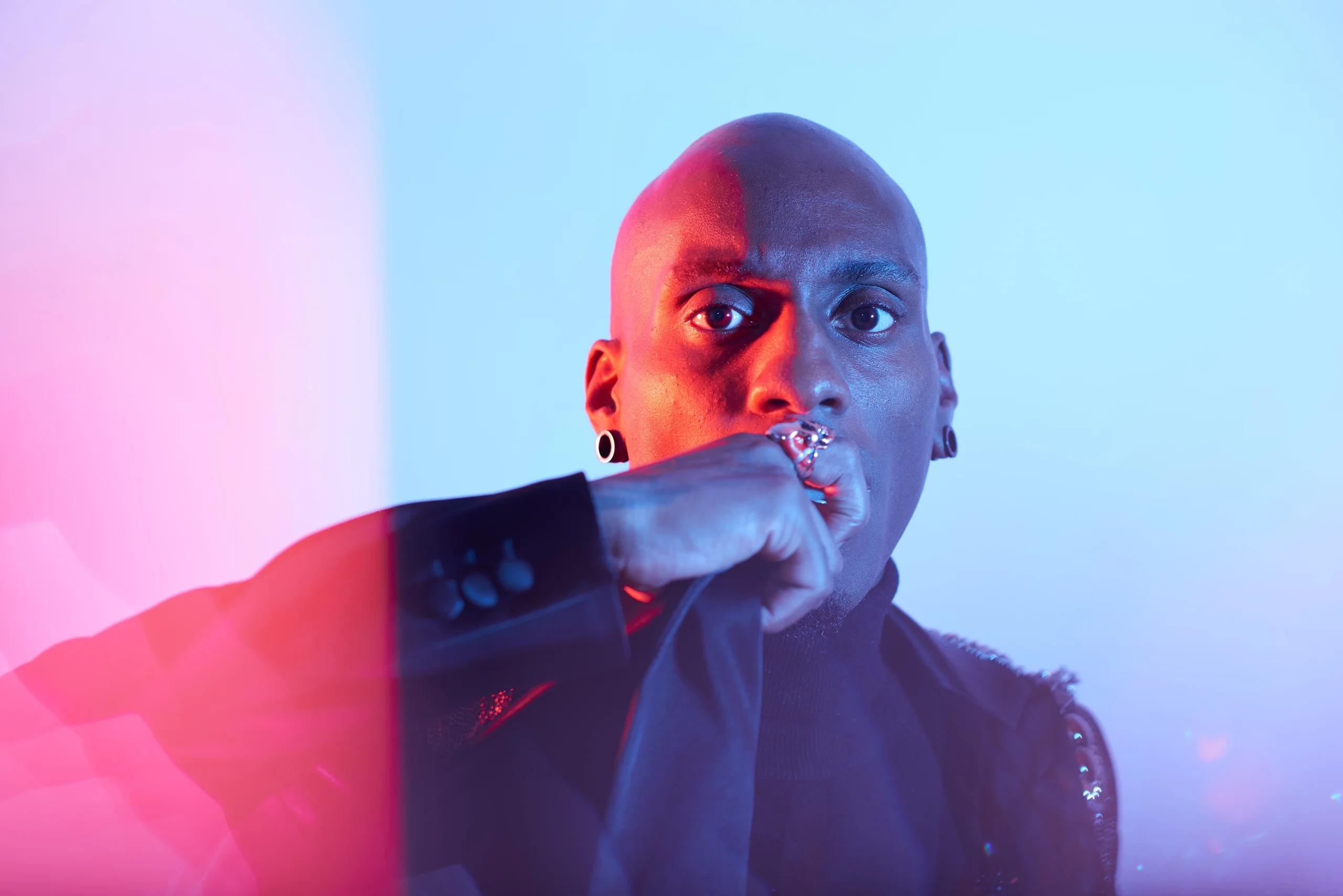 A close portrait with a bent arm across the lower face and blue and pink light.