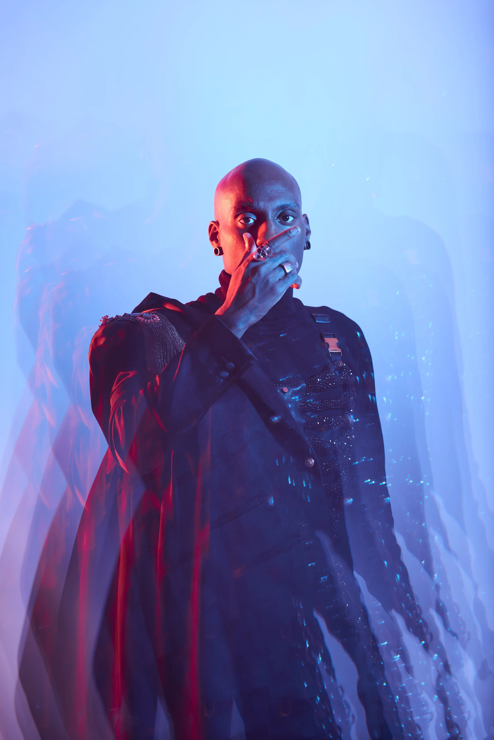 A front-facing figure in a dark jacket with repeated silhouettes in blue and red light.