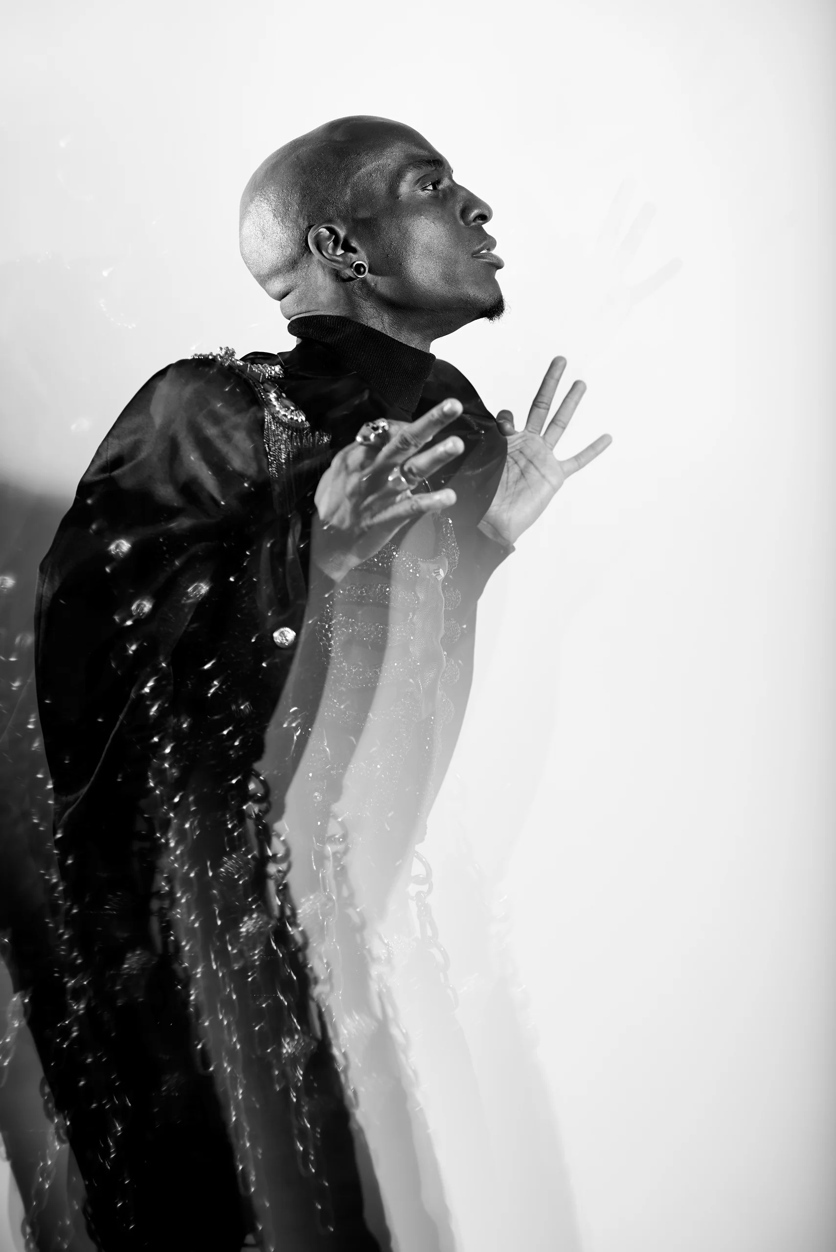 A black-and-white profile with raised hands and a blurred trail along a dark jacket.