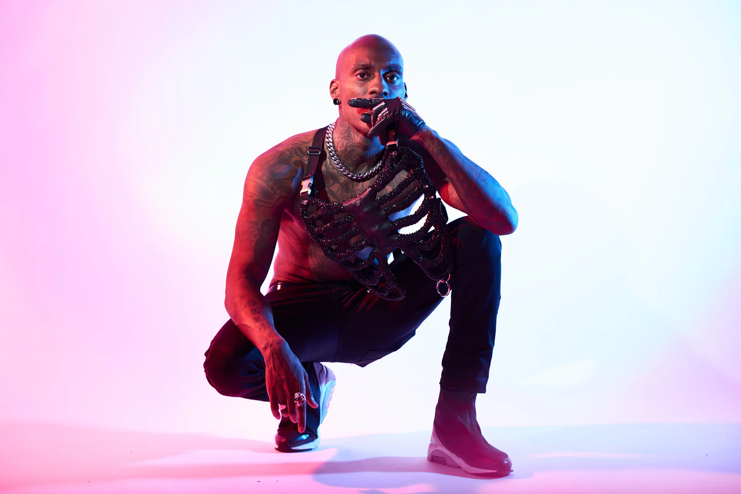 A figure crouching low with one hand near the face against a pink and blue background.