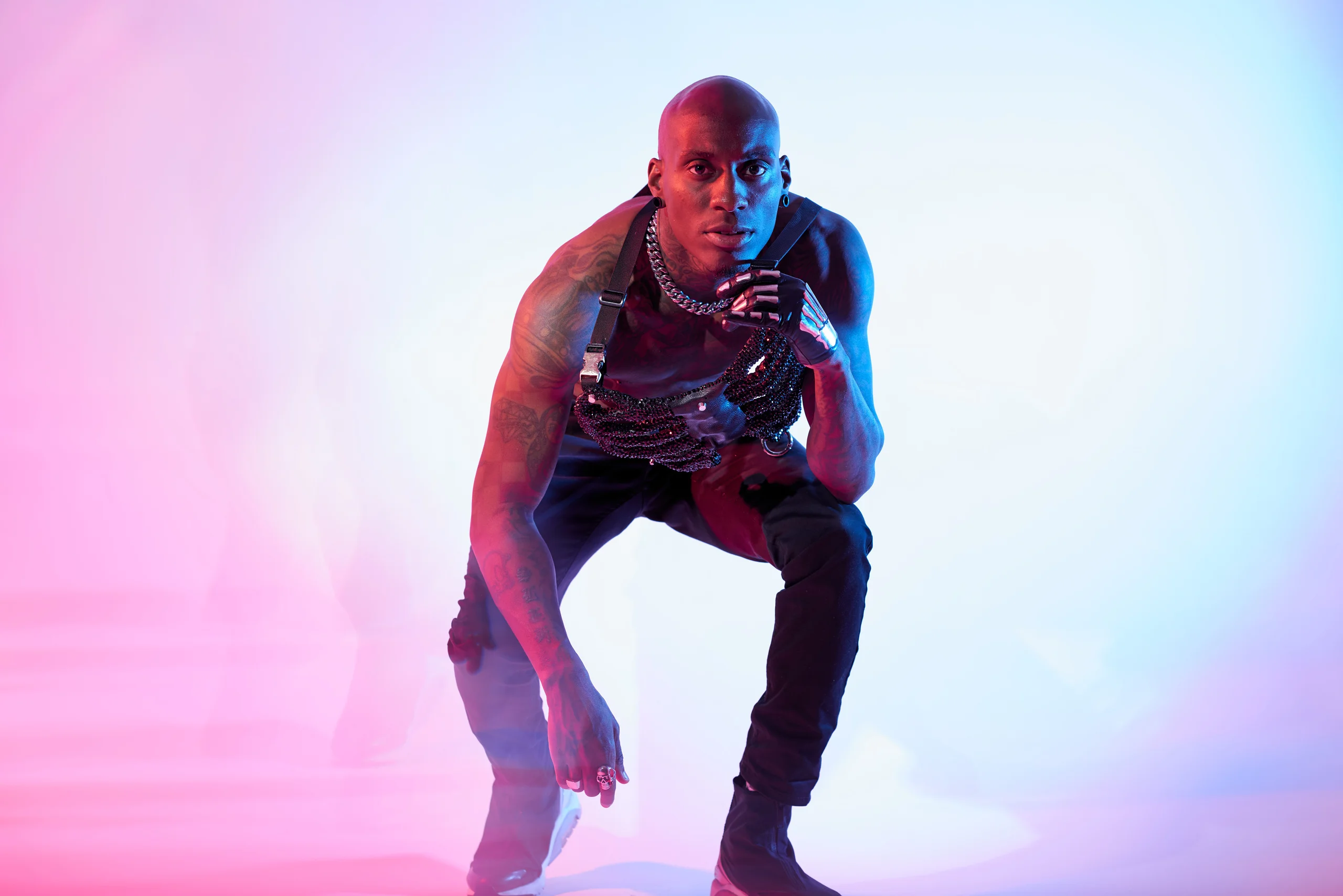 A figure leaning forward from a squat with a hand near the chin against pastel light.