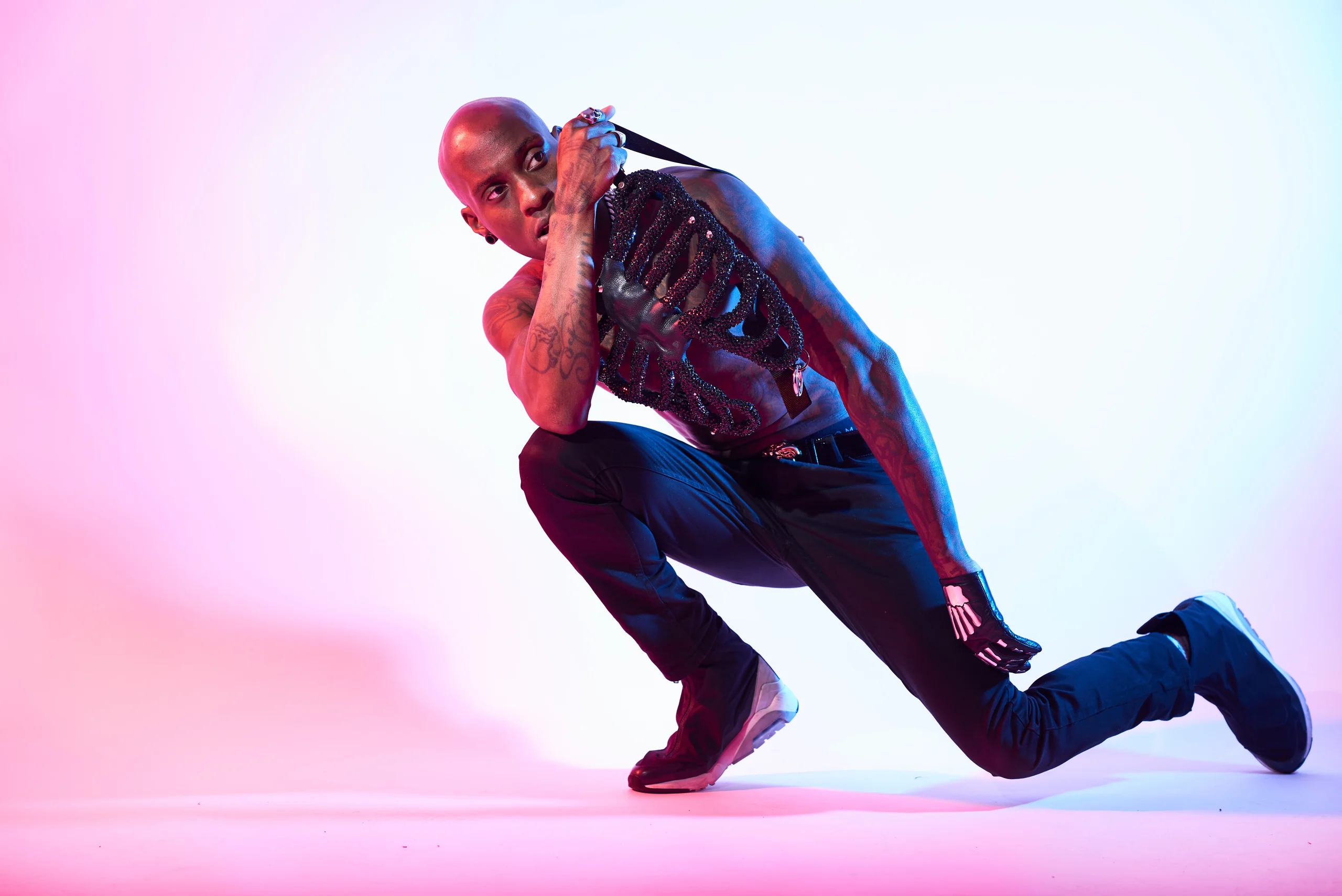 A figure balancing low on one leg, with the other leg stretched behind, under pink and blue light.