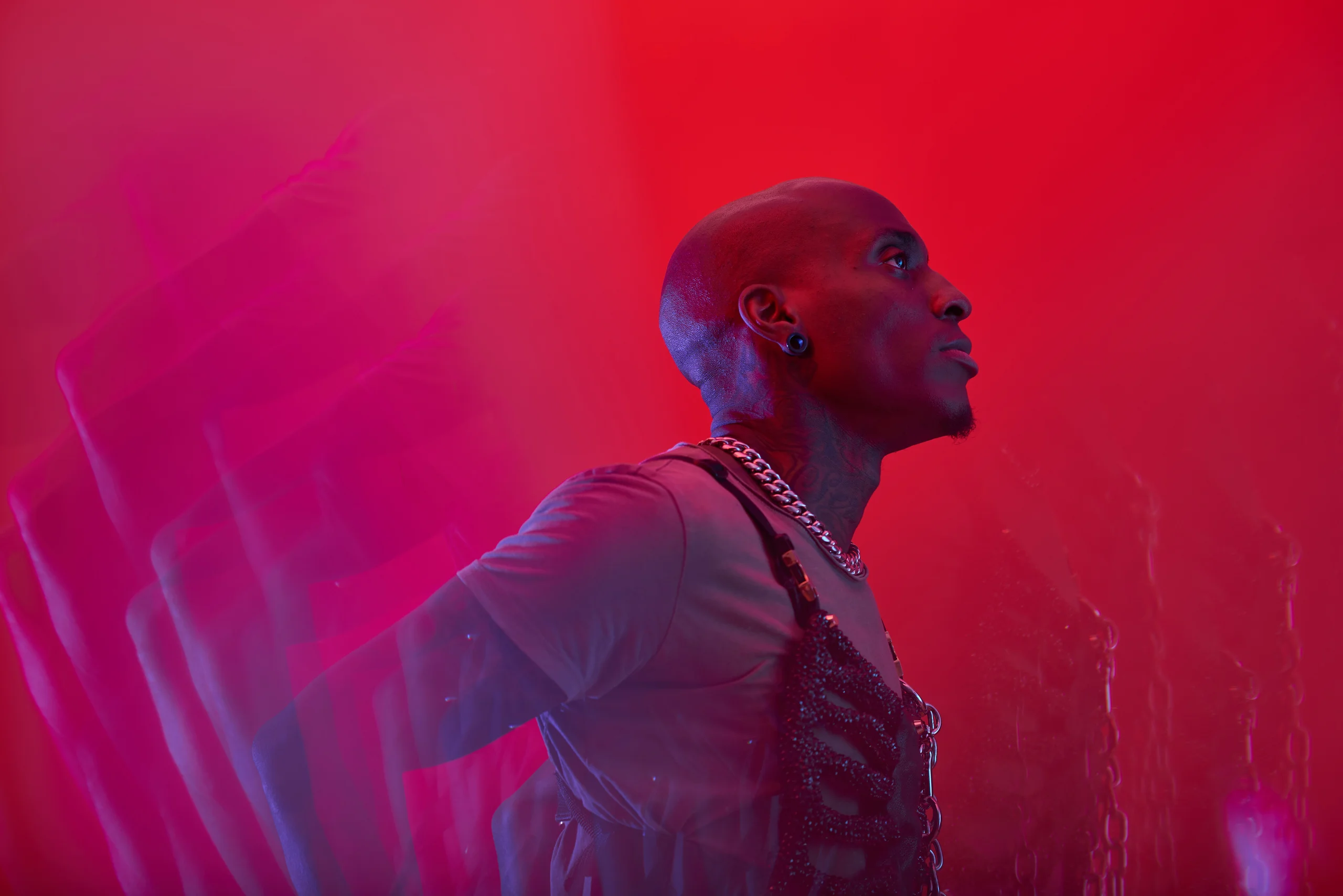A figure looking upward in profile, with chains across the shoulders and red light trails.