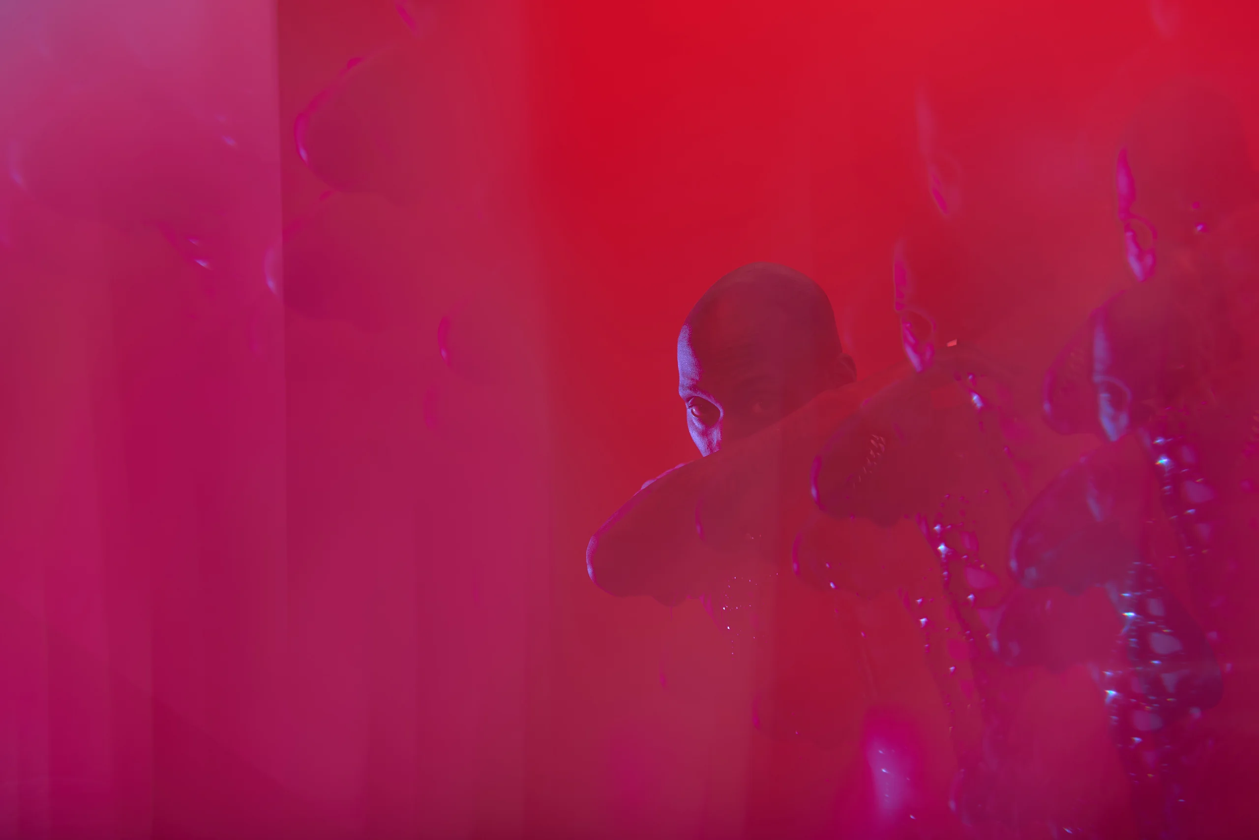 A shadowed figure partly obscured by layered red and magenta reflections.