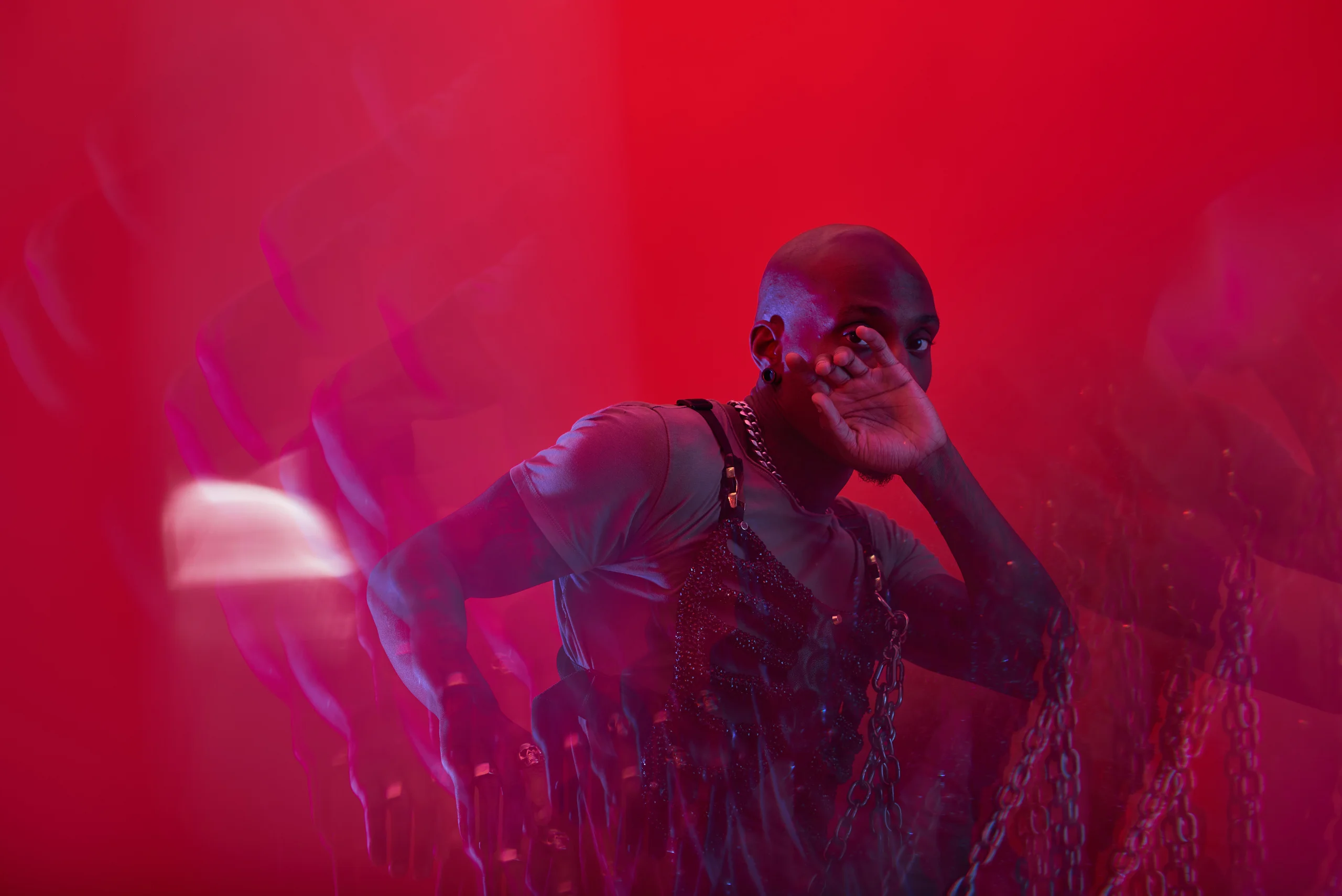 A figure extending one arm while holding the other hand near the face under red light.