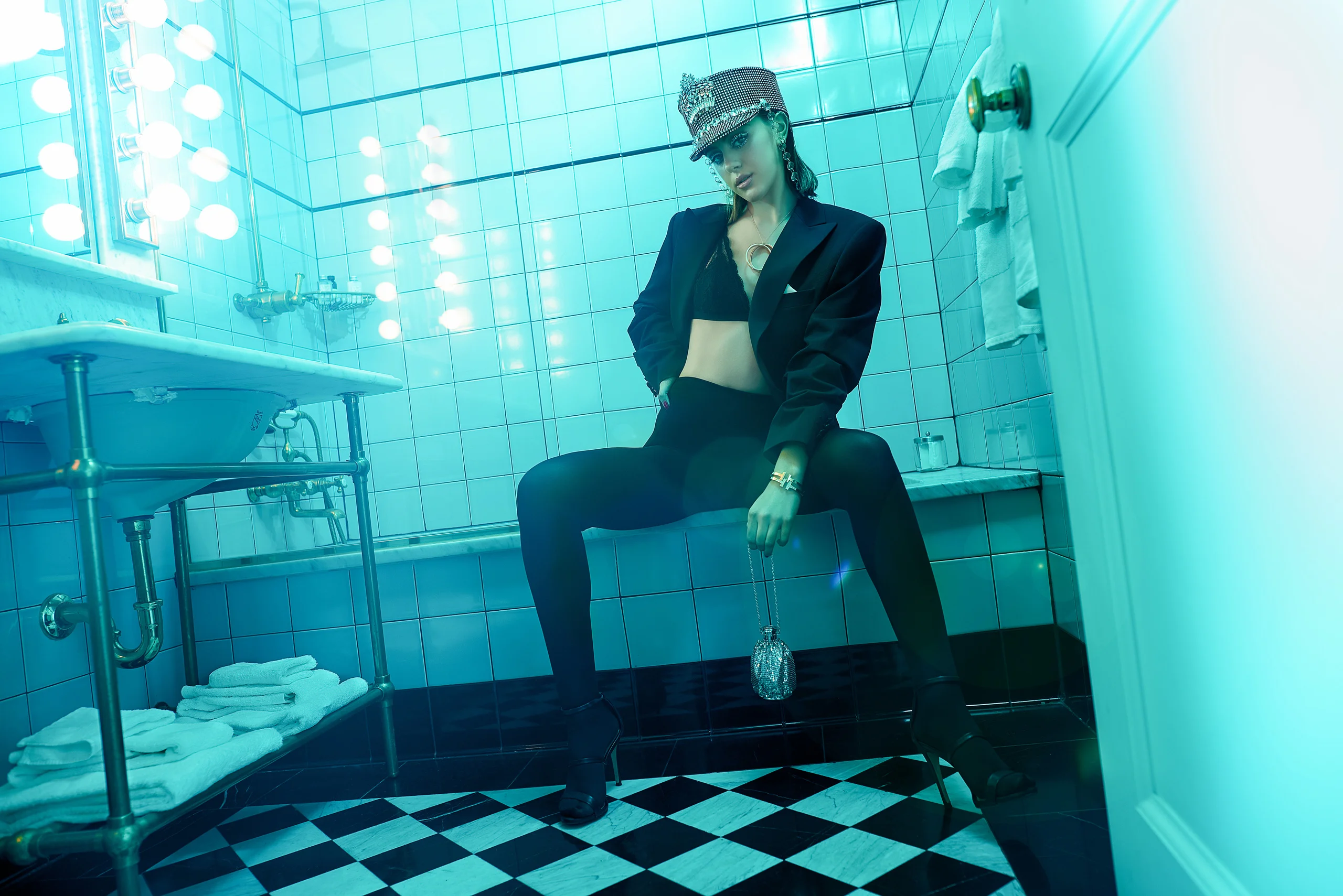 A model in a dark suit seated in a tiled room under turquoise light.