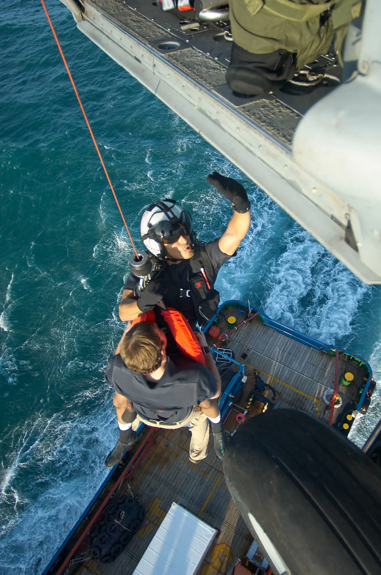 A helmeted person and equipment suspended beside an aircraft doorway above water.