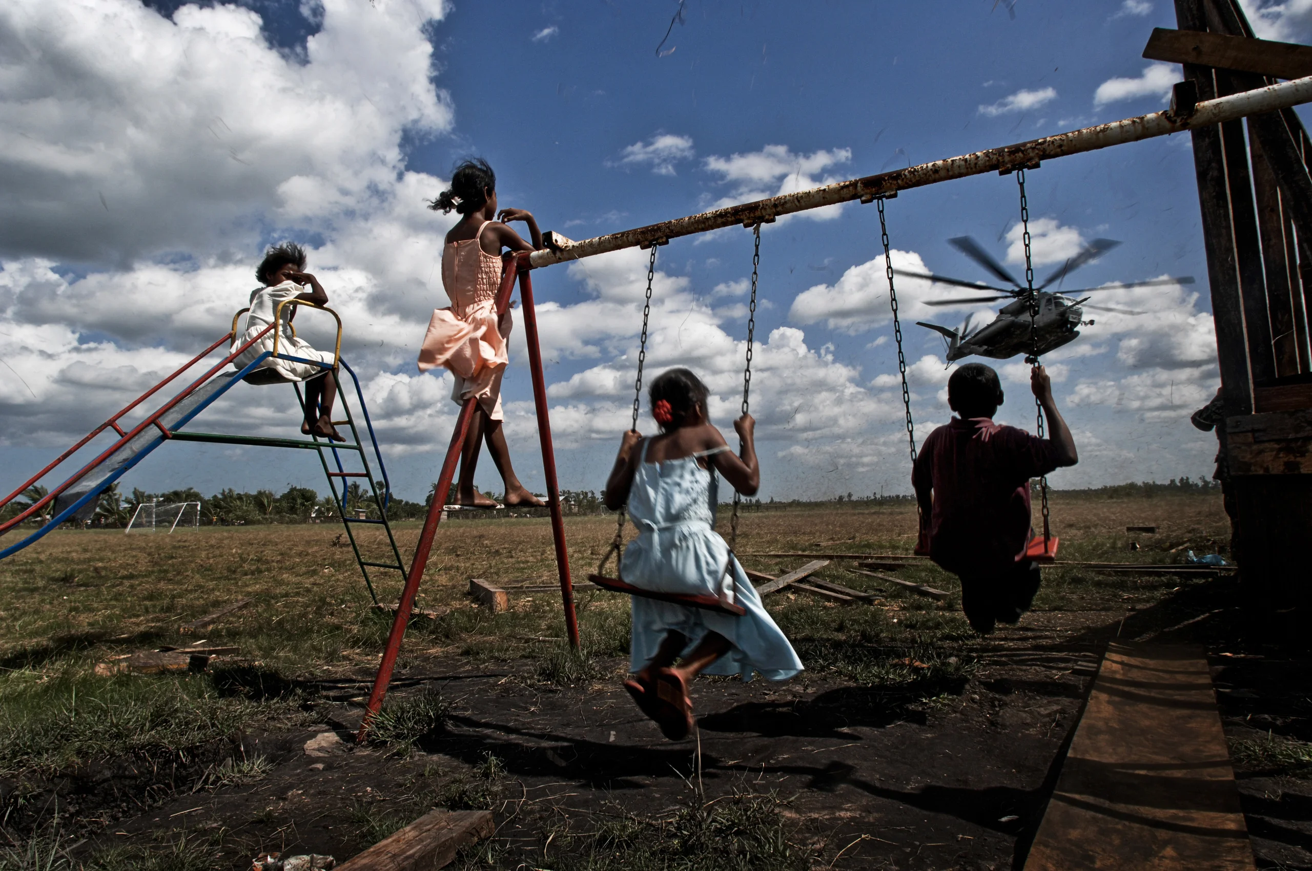 Children playing on a swing set with a helicopter in the background.