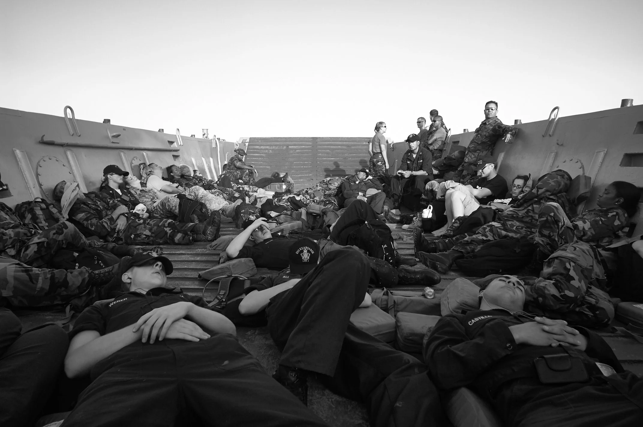 A black-and-white view of people reclining among bags inside a landing craft.