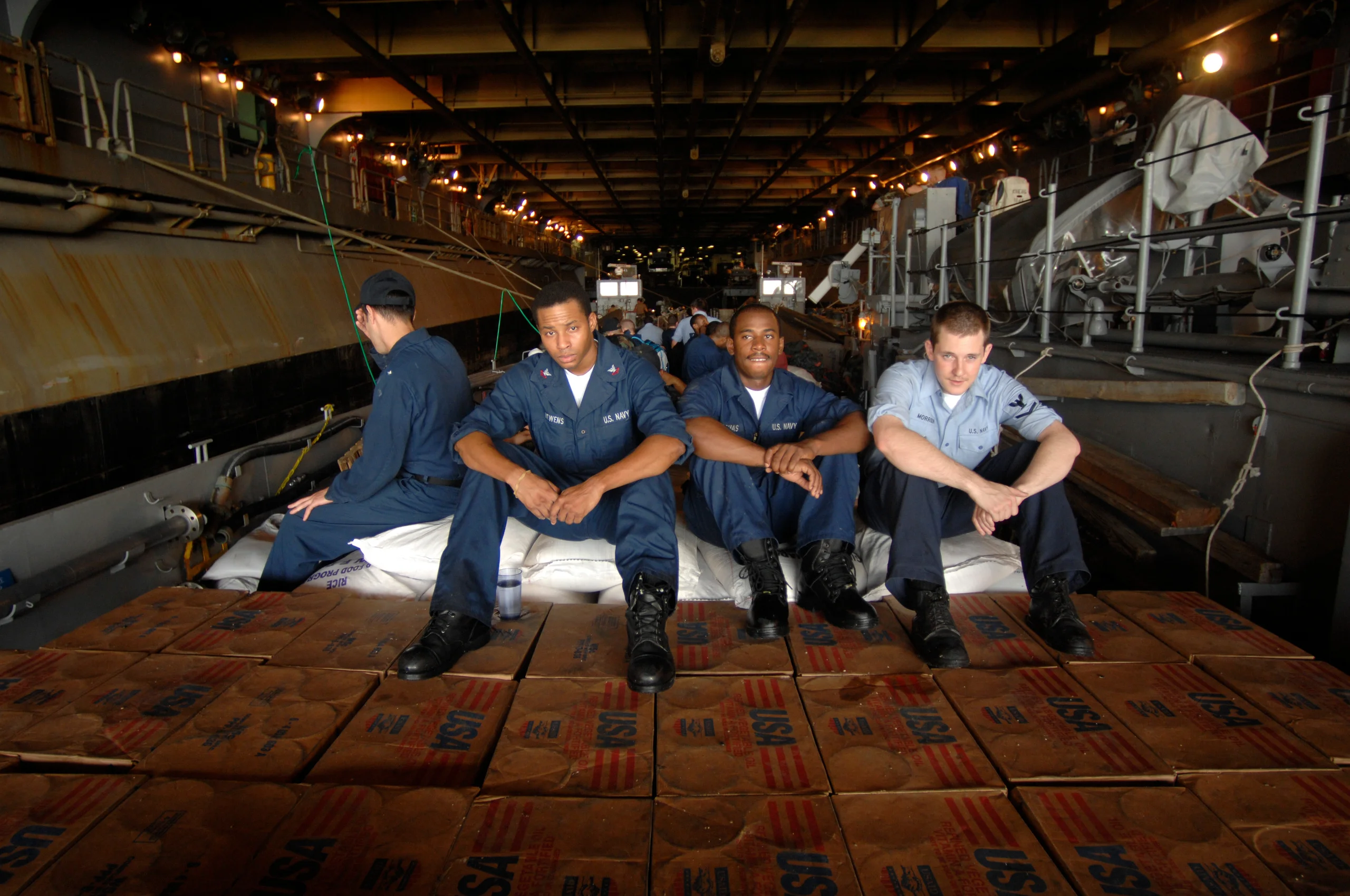 Five people sitting together in work clothes inside a large industrial interior.