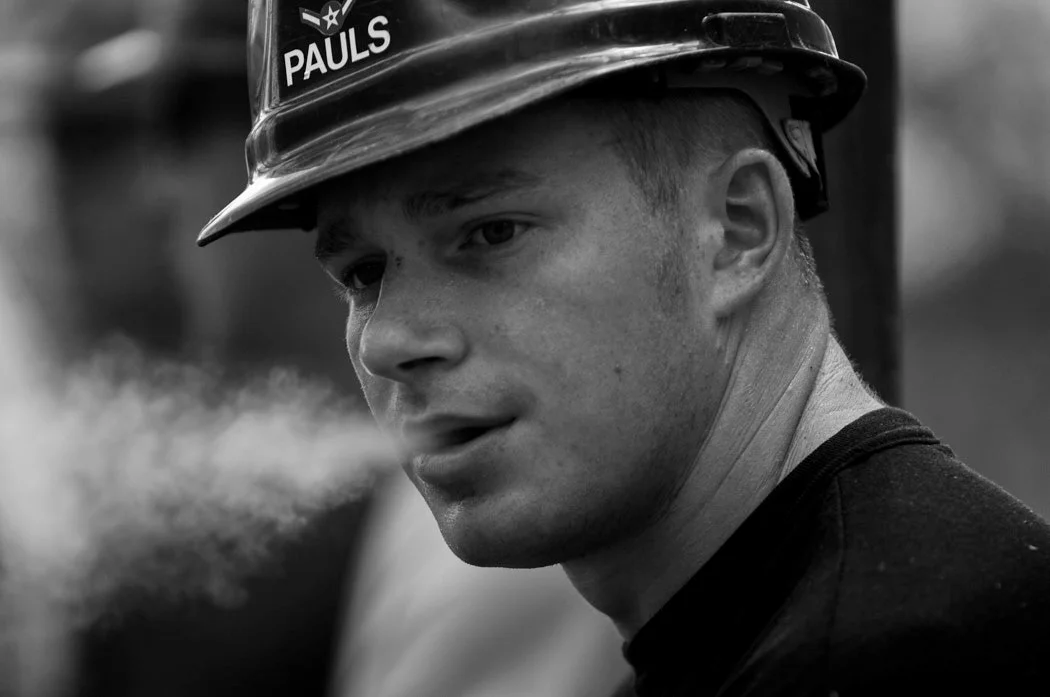 A black-and-white close portrait of a person in a hard hat.