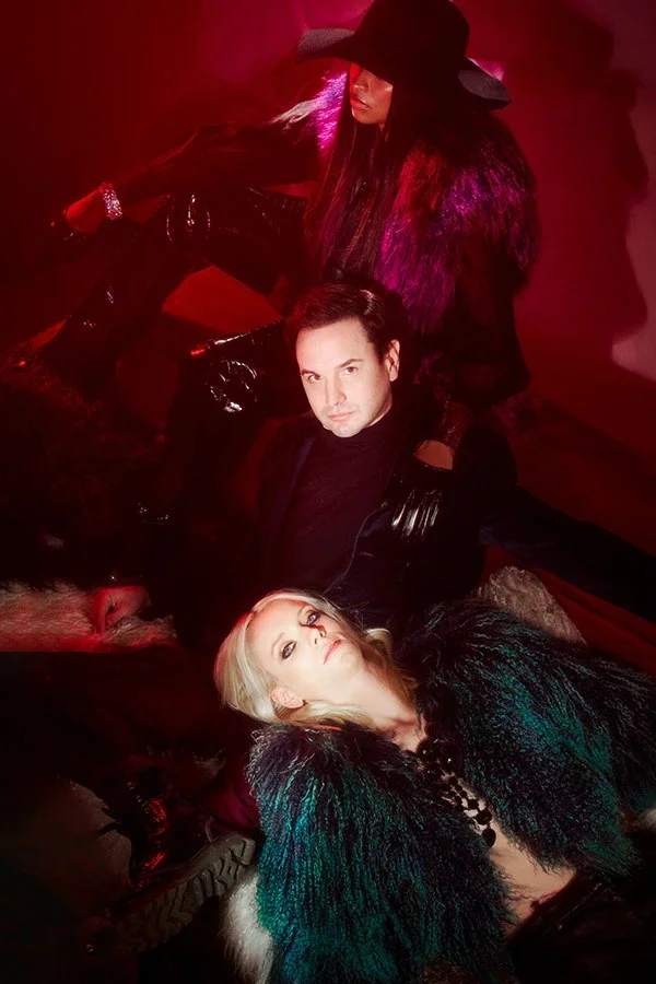 Three models posed at different heights in dark clothing under deep red light.
