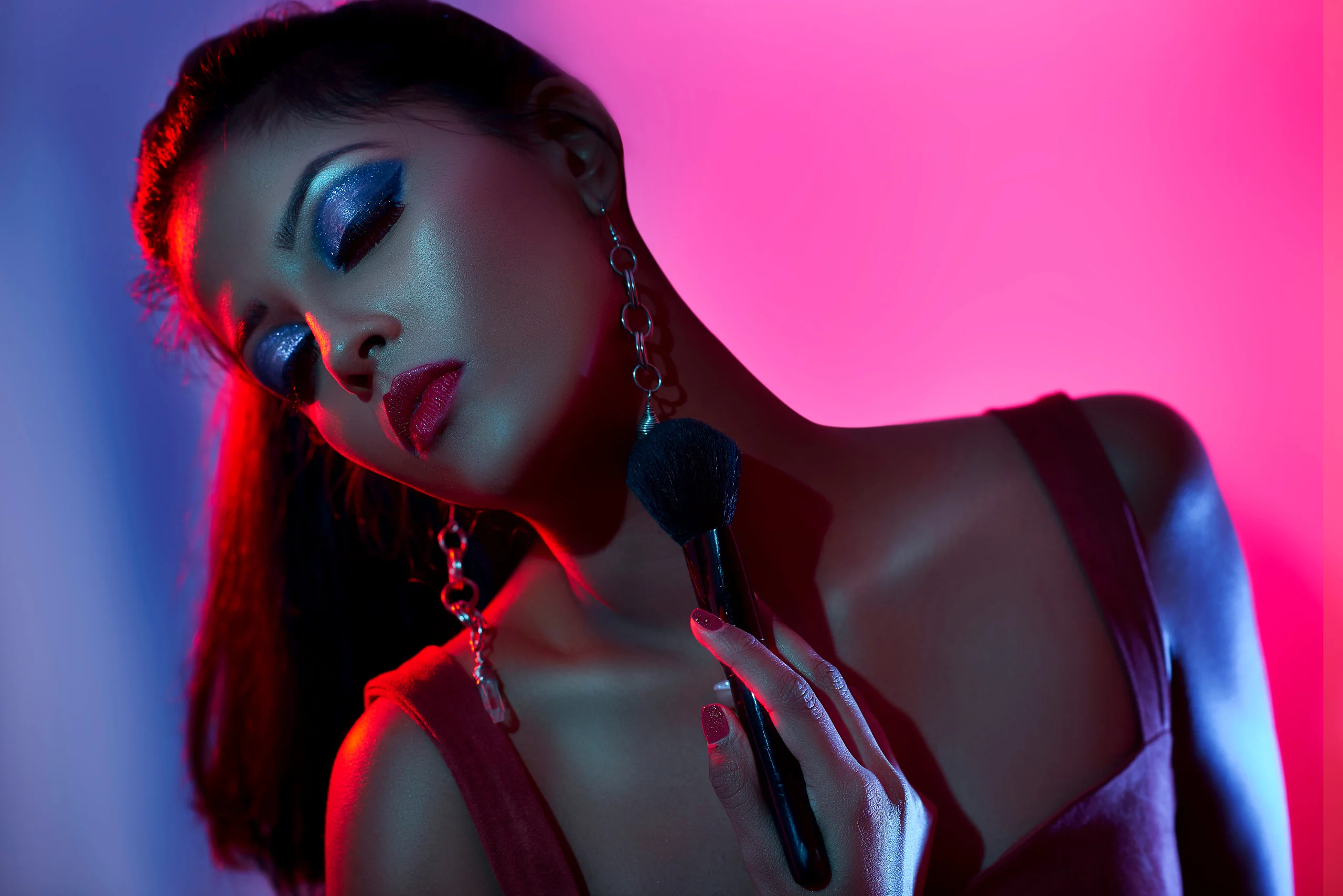 A model with blue eye makeup and long earrings against a bright pink background.