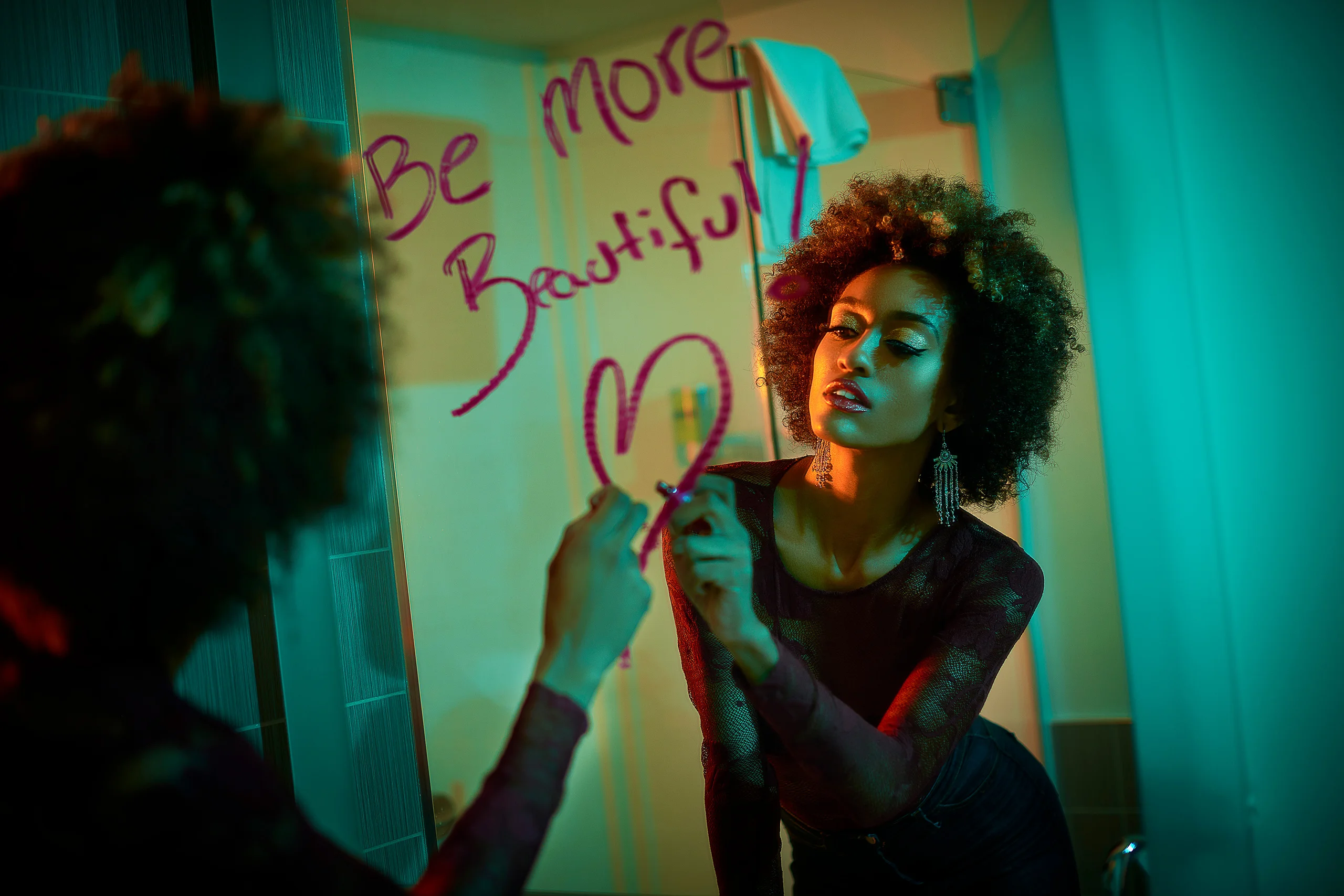 A model writing on a mirror while facing their reflection under teal light.
