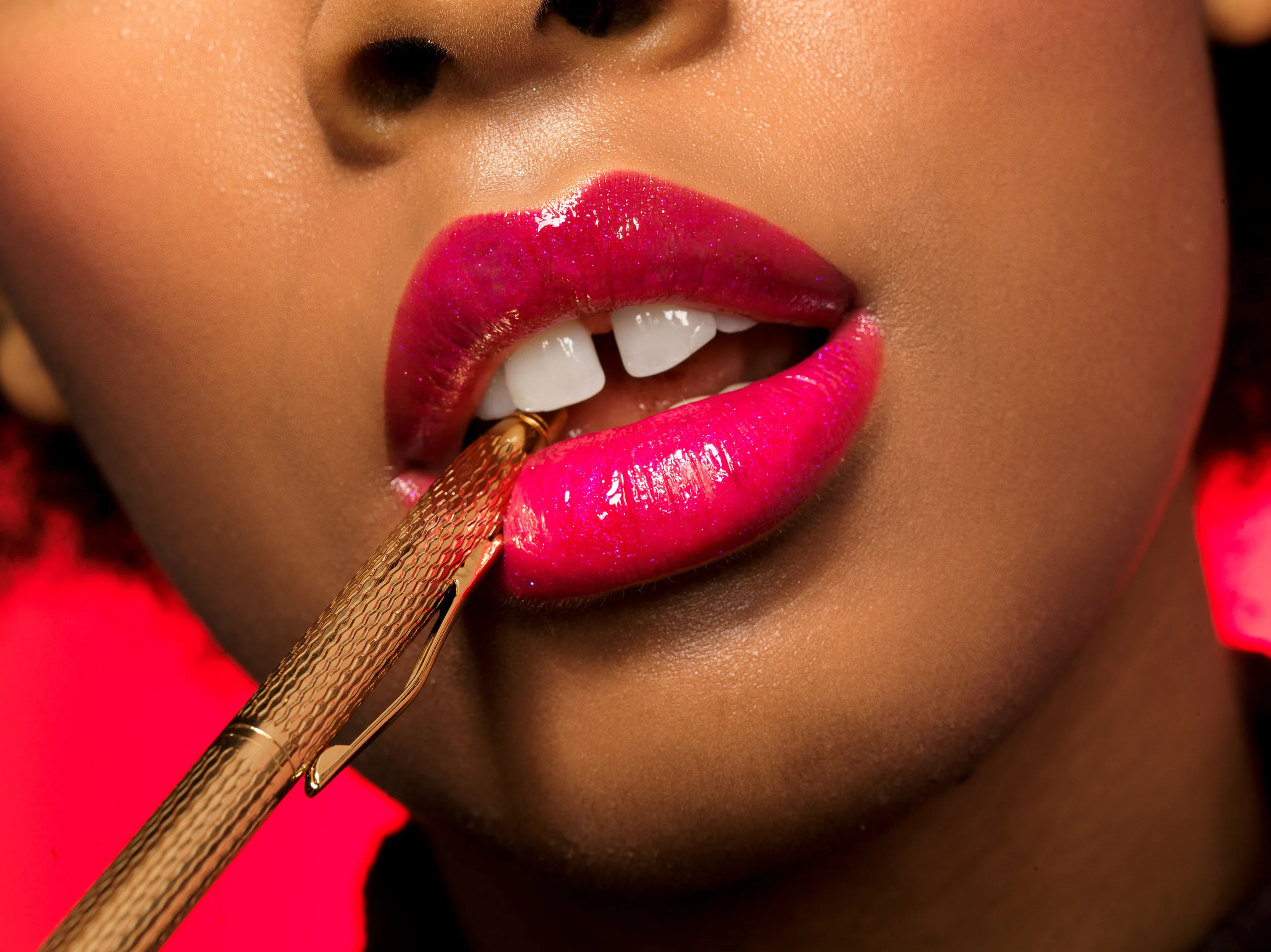 A close-up of glossy pink lips holding the edge of a gold object.