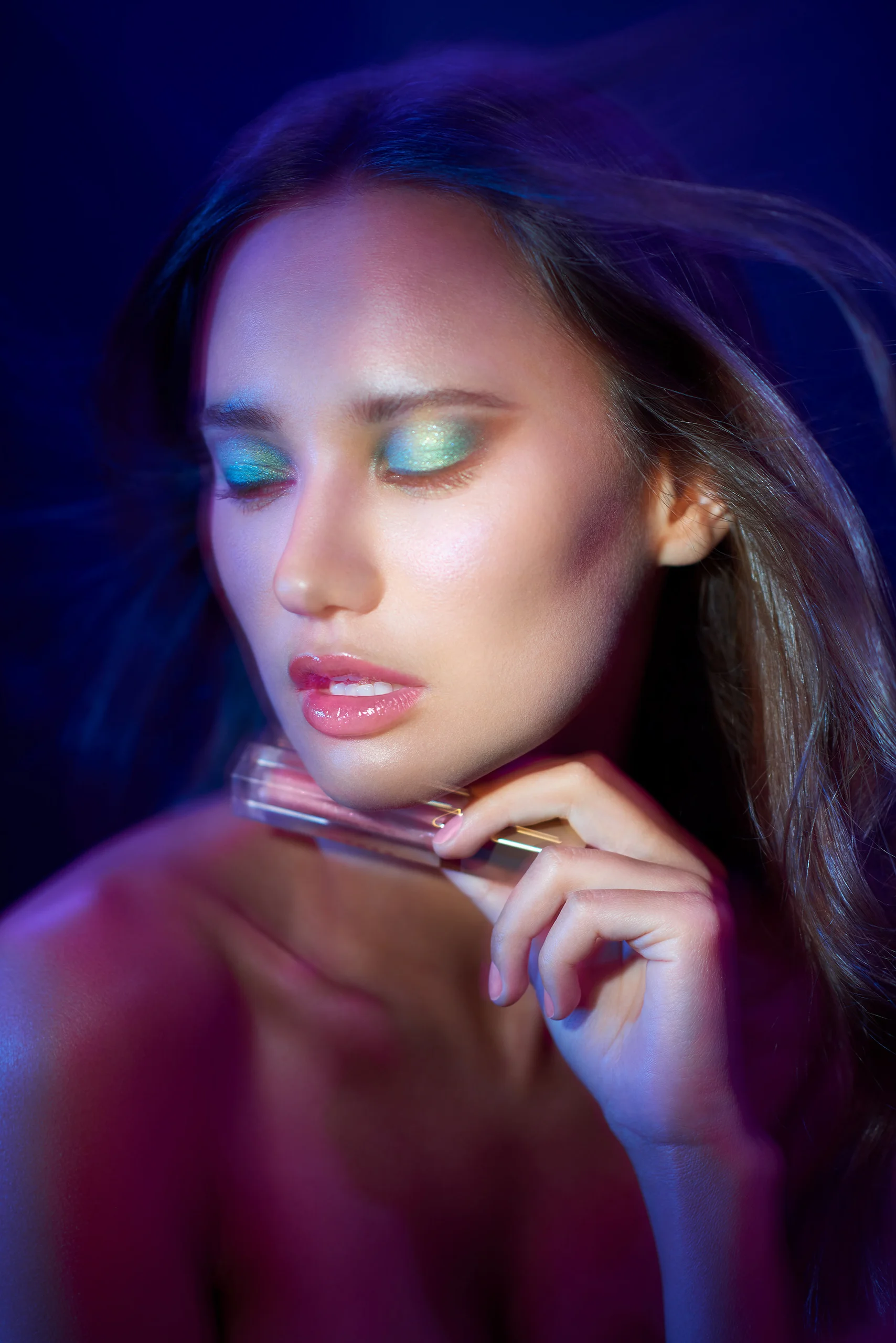A beauty portrait with shimmering eye makeup under violet and blue light.
