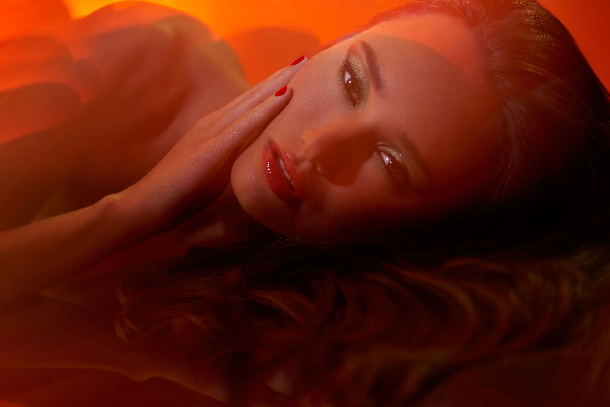 A reclining beauty portrait in warm orange light.