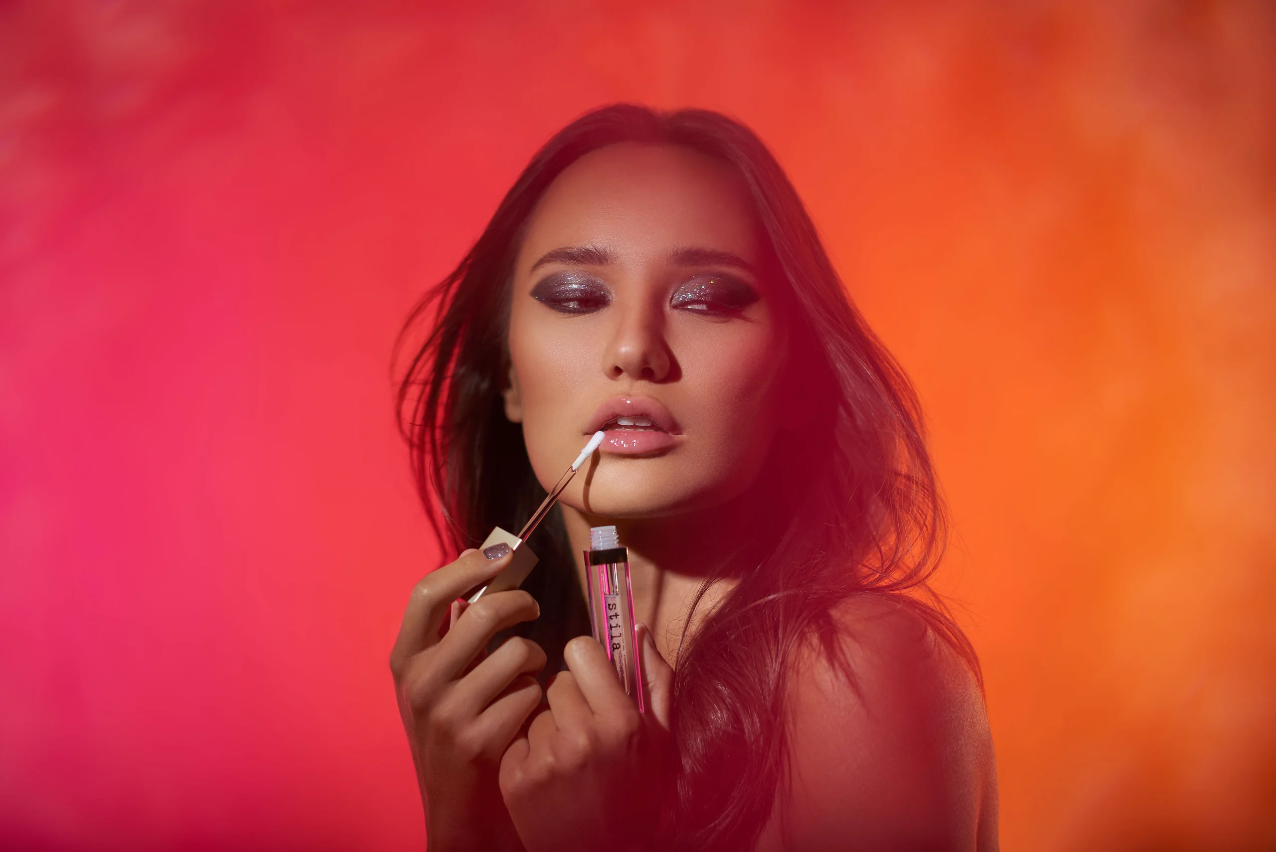 A model applies lip color against orange and magenta haze.